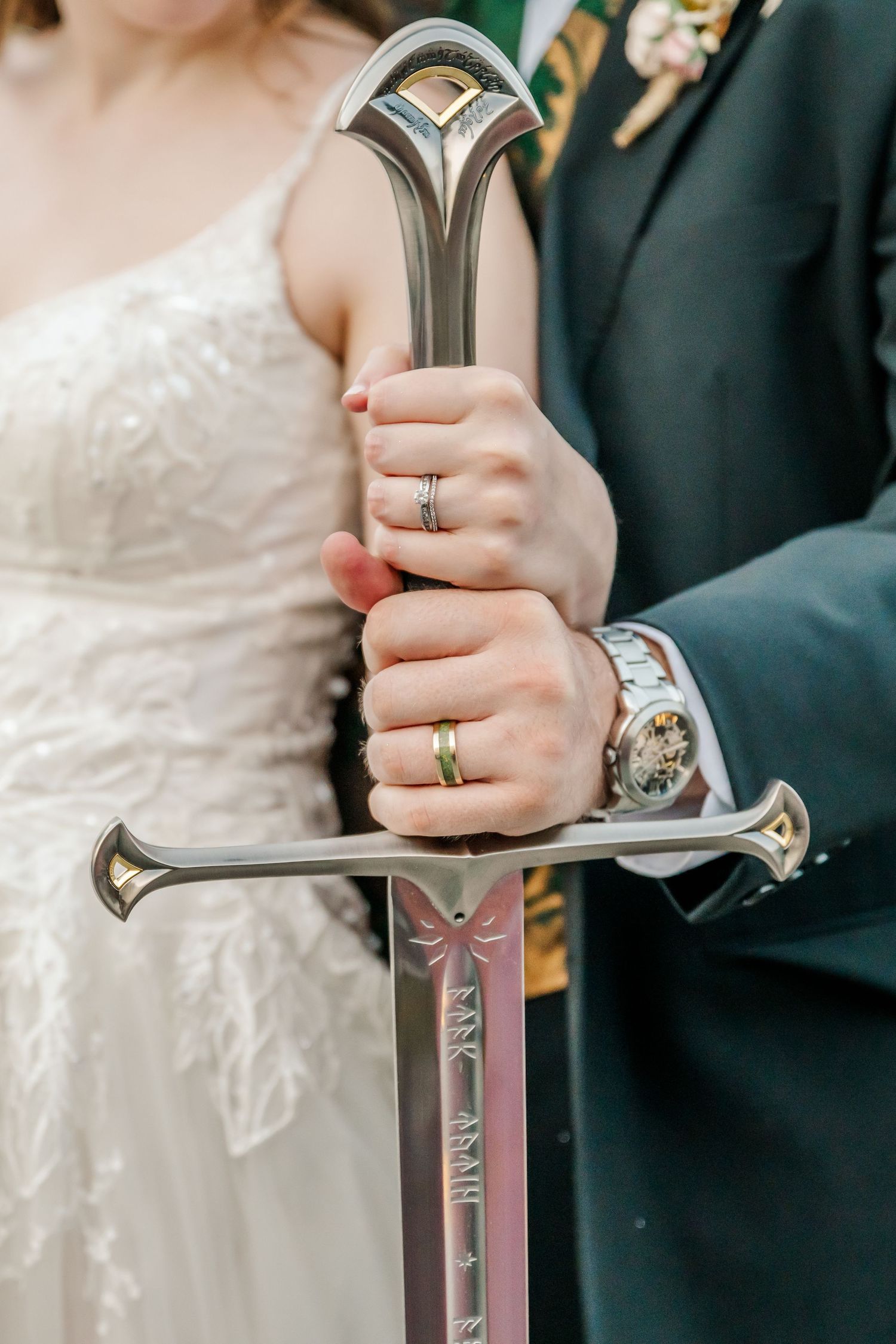 Close-up of hands holding a ceremonial sword showing matching wedding rings and formal attire.