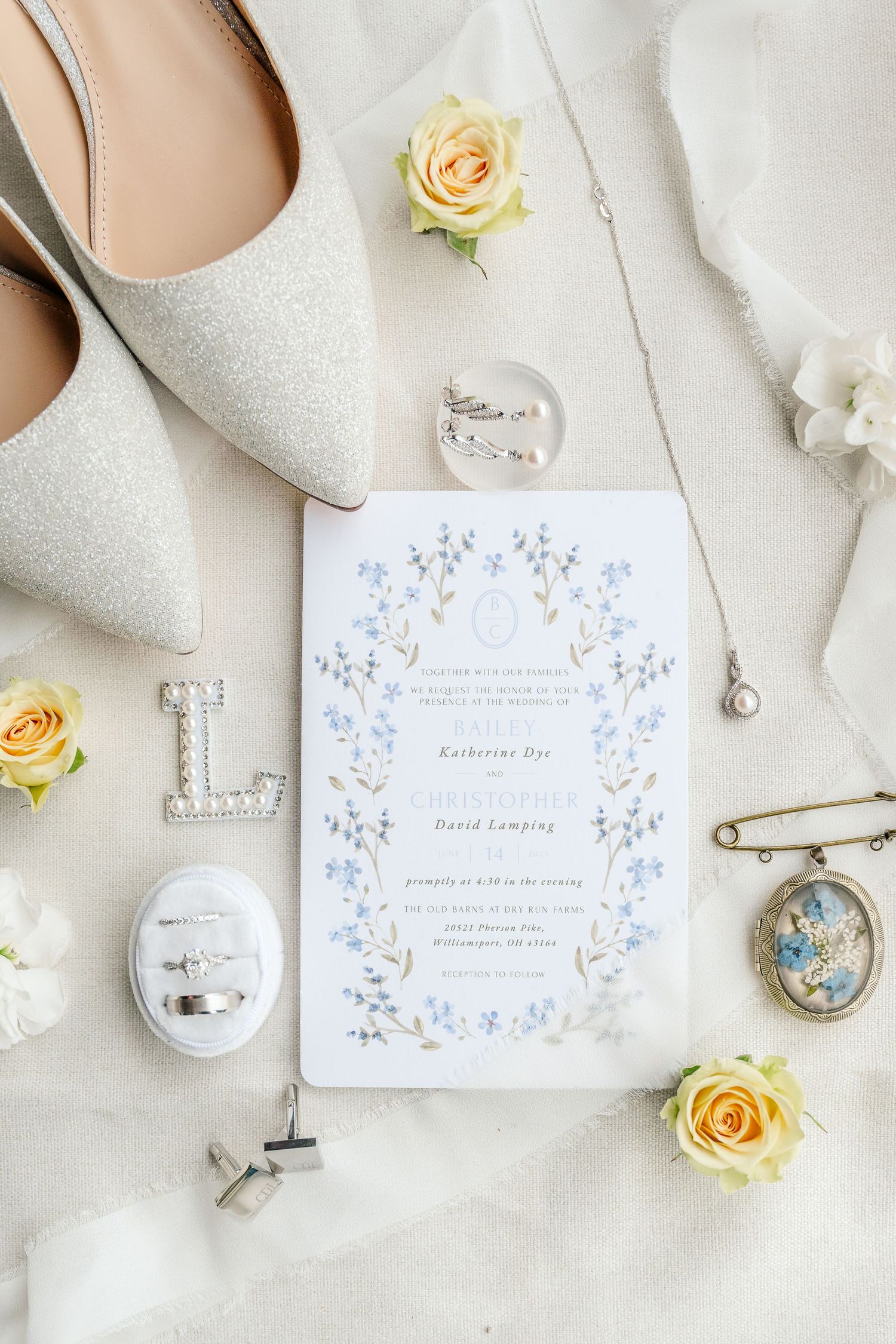 Elegant wedding details flatlay with white shoes, yellow roses, and delicate blue floral stationery on light background.