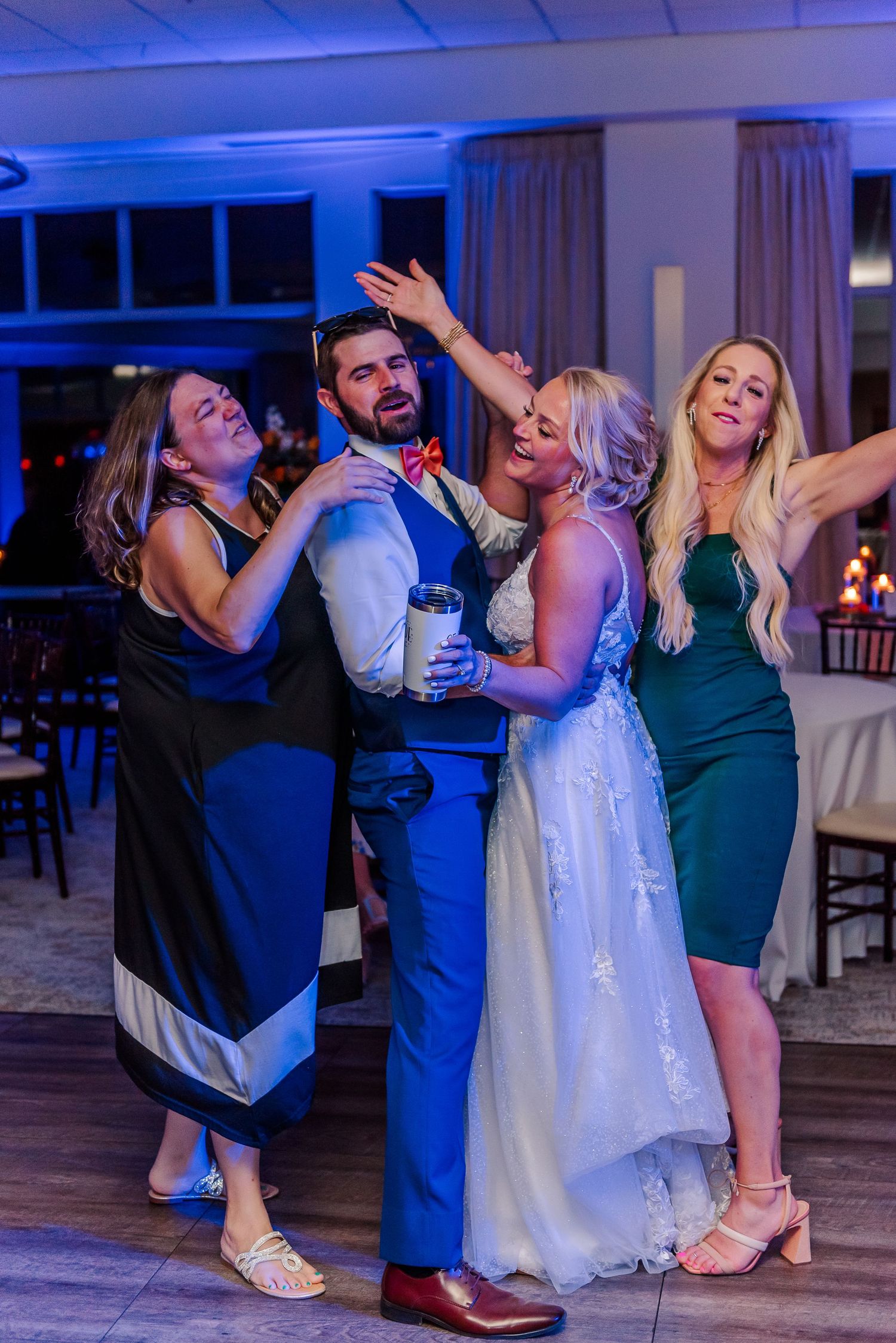 Wedding party members pose playfully on the dance floor under blue lighting at an evening reception.