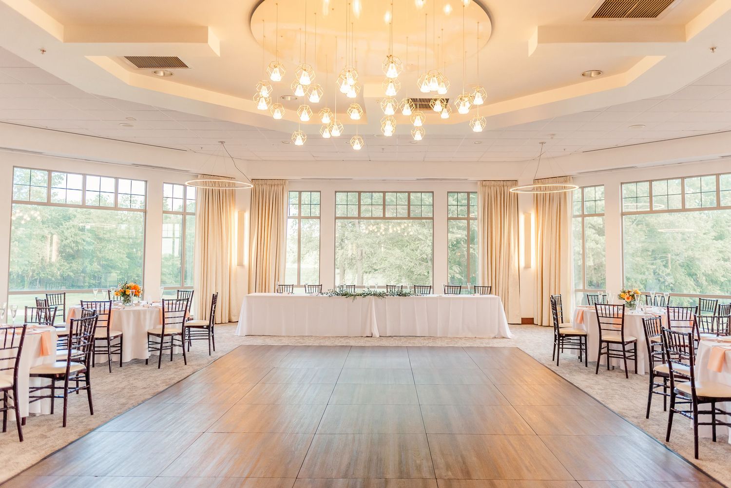 Elegant ballroom with panoramic windows, crystal chandeliers, and hardwood floors in a bright, airy event space.