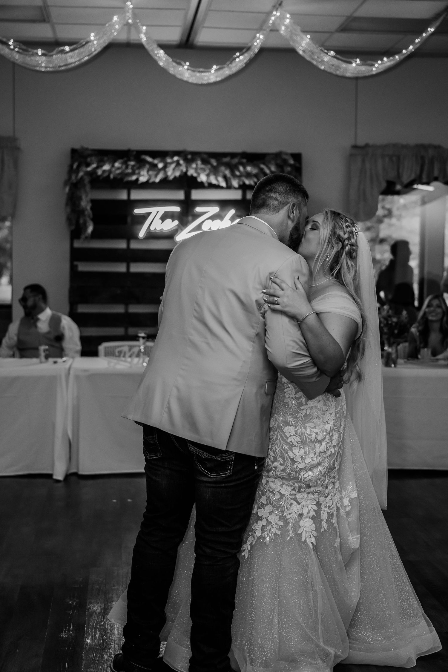 A couple shares a tender dance moment at a wedding reception with string lights glowing overhead.