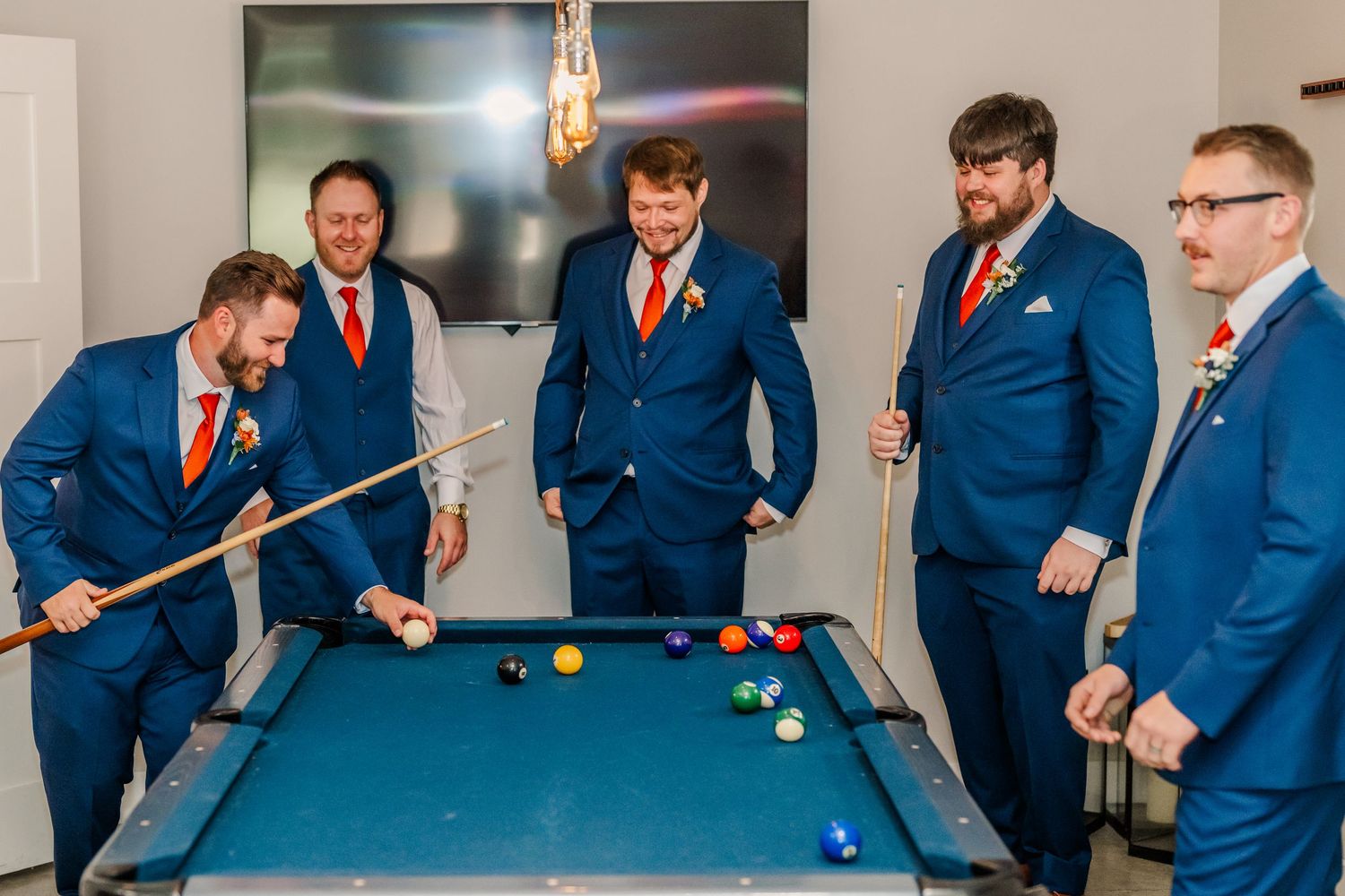 Groomsmen in blue suits play pool together at a wedding venue, showing playful moments during pre-ceremony activities