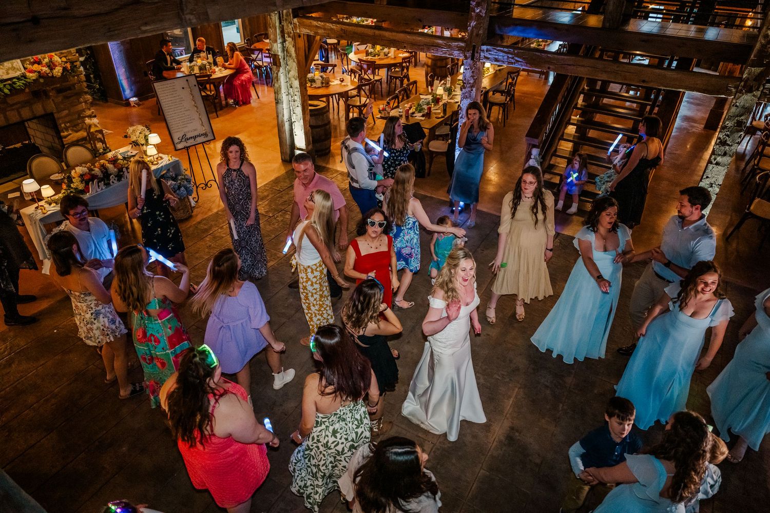 Large group of wedding guests dancing and celebrating on a dimly lit dance floor at reception.