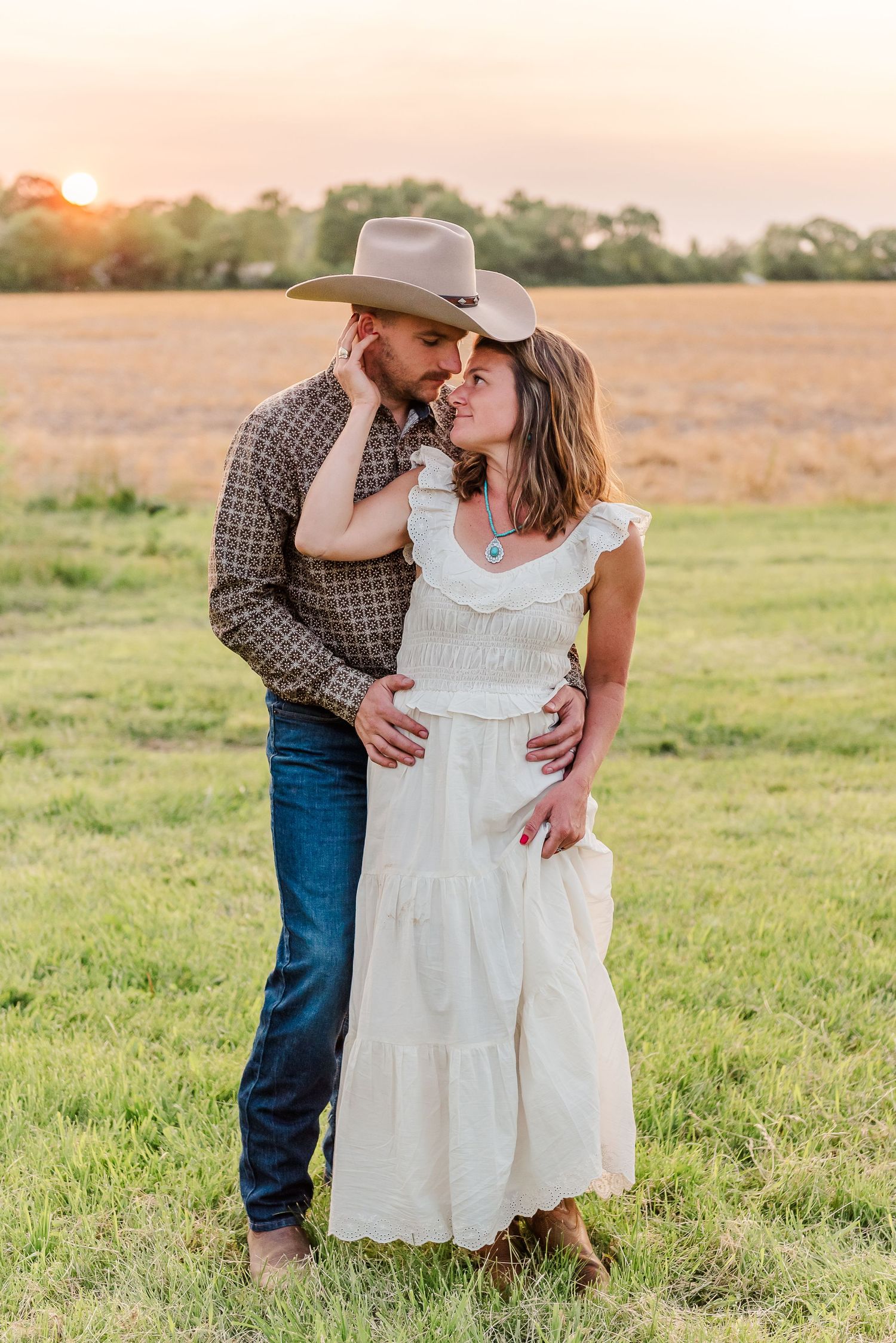 Romantic couple in cowboy attire share tender moments in a sunlit field at golden hour.