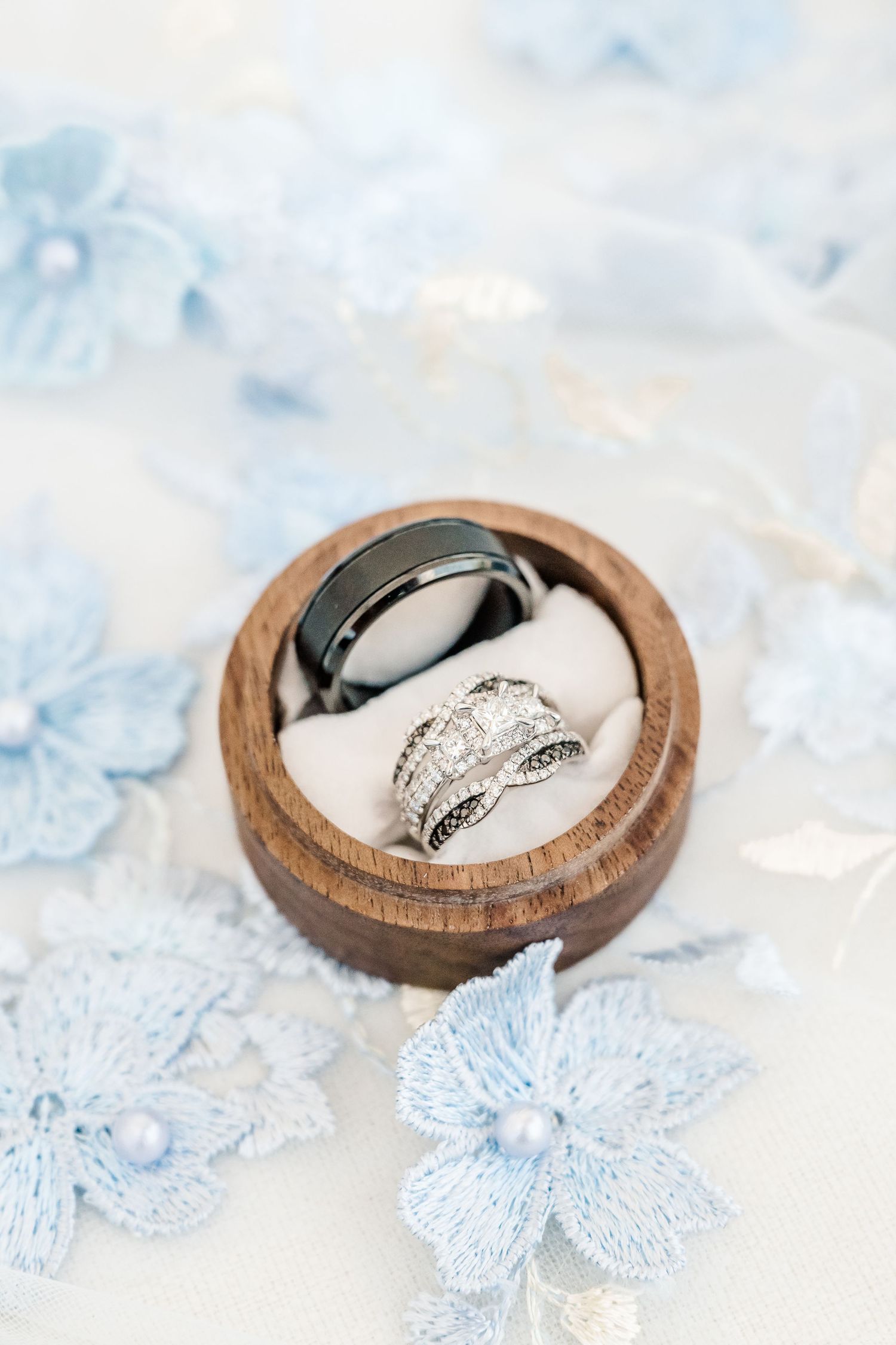 Wedding rings nestled in small wooden ring boxes surrounded by delicate blue floral lace details.
