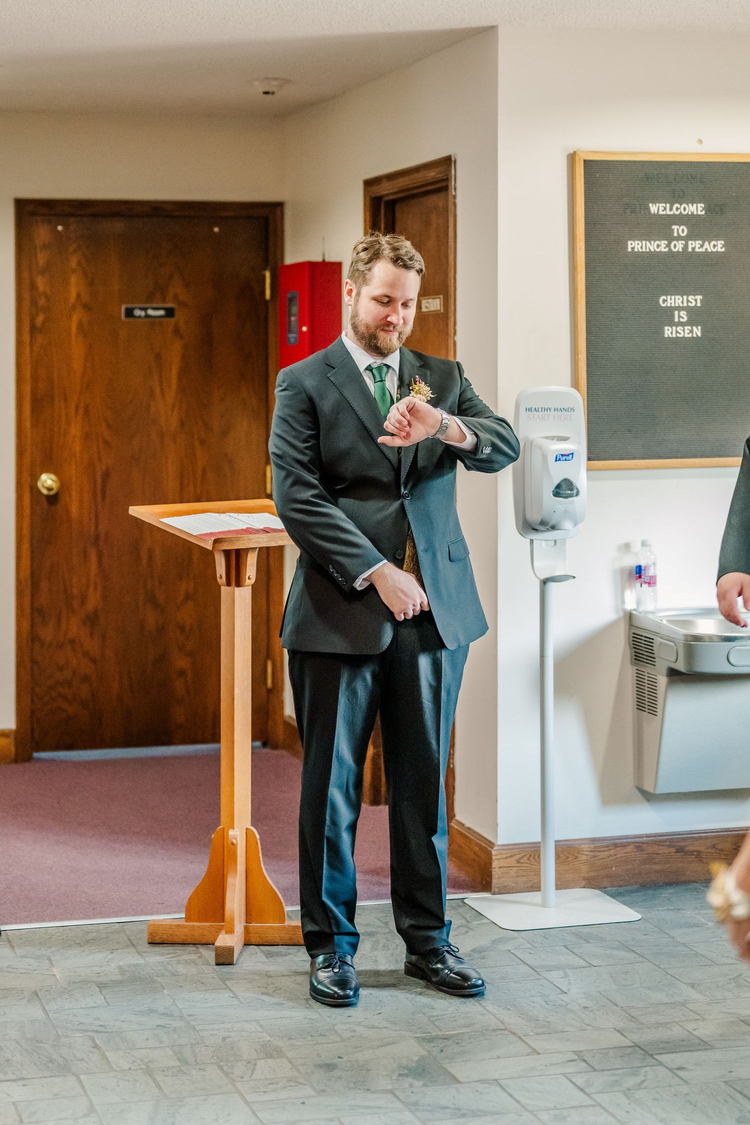 Wedding party member in formal attire adjusting their suit in church hallway.
