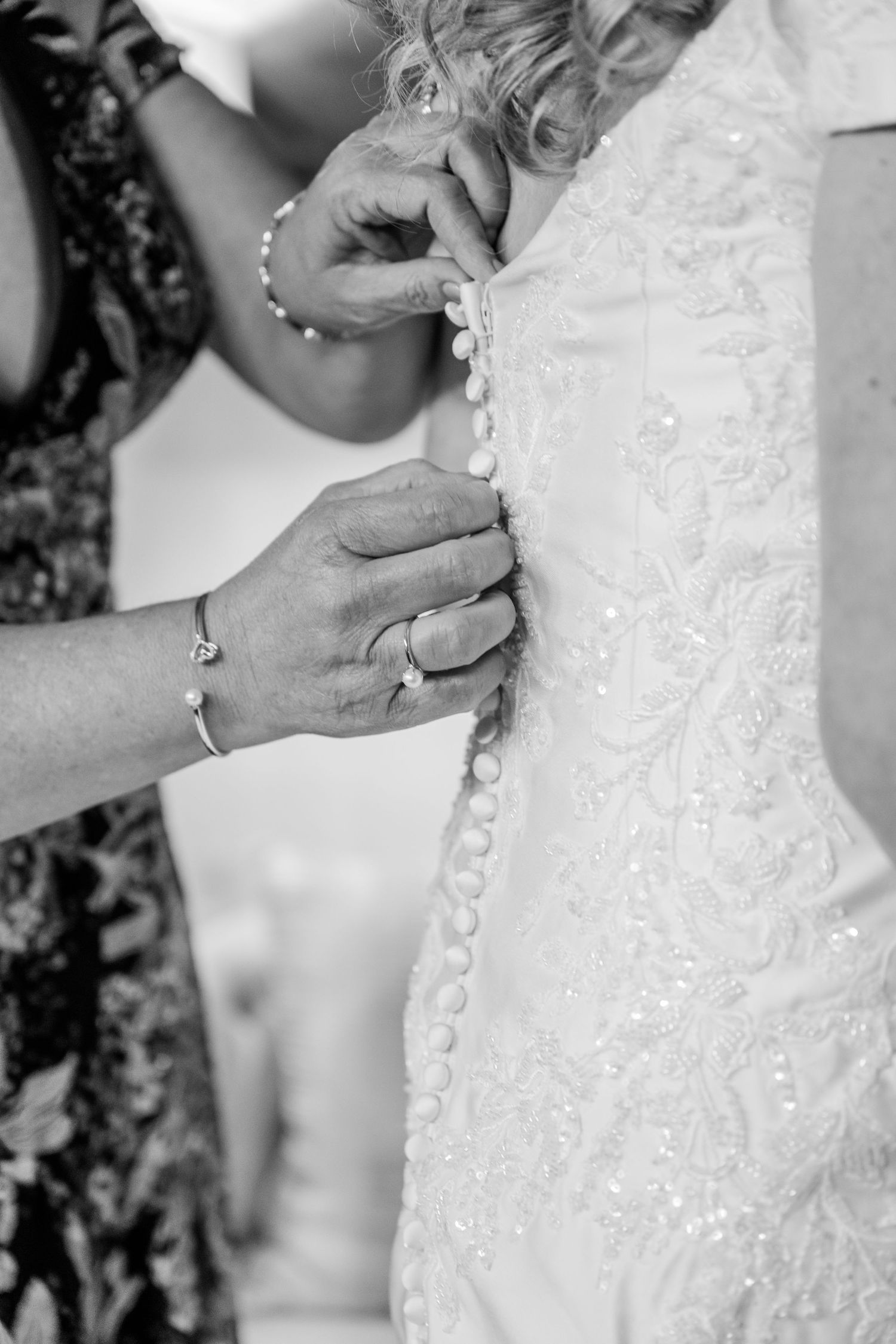 Close-up black and white detail of hands buttoning an ornate lace wedding dress. The Old Barns at Dry Run Farms in Williamsport, OH.