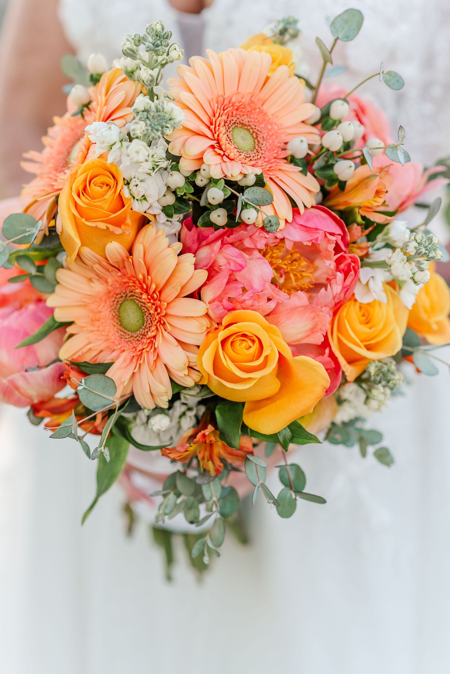 A vibrant wedding bouquet with peach gerbera daisies, orange roses, pink flowers, and eucalyptus greenery.