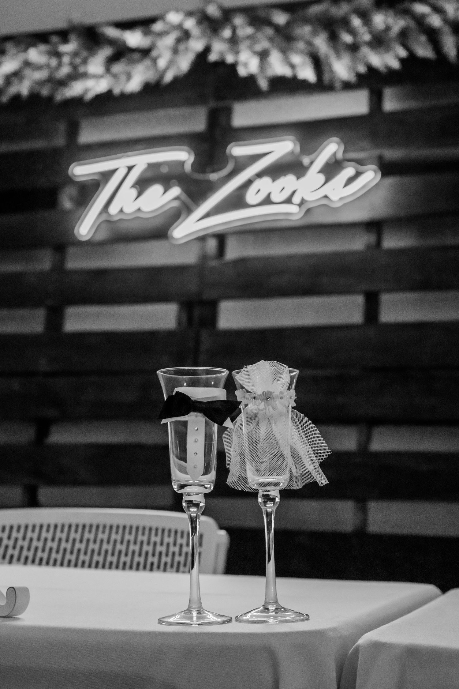 Two elegant cocktail glasses sit on a white tablecloth beneath vintage neon signage in a dimly lit venue.