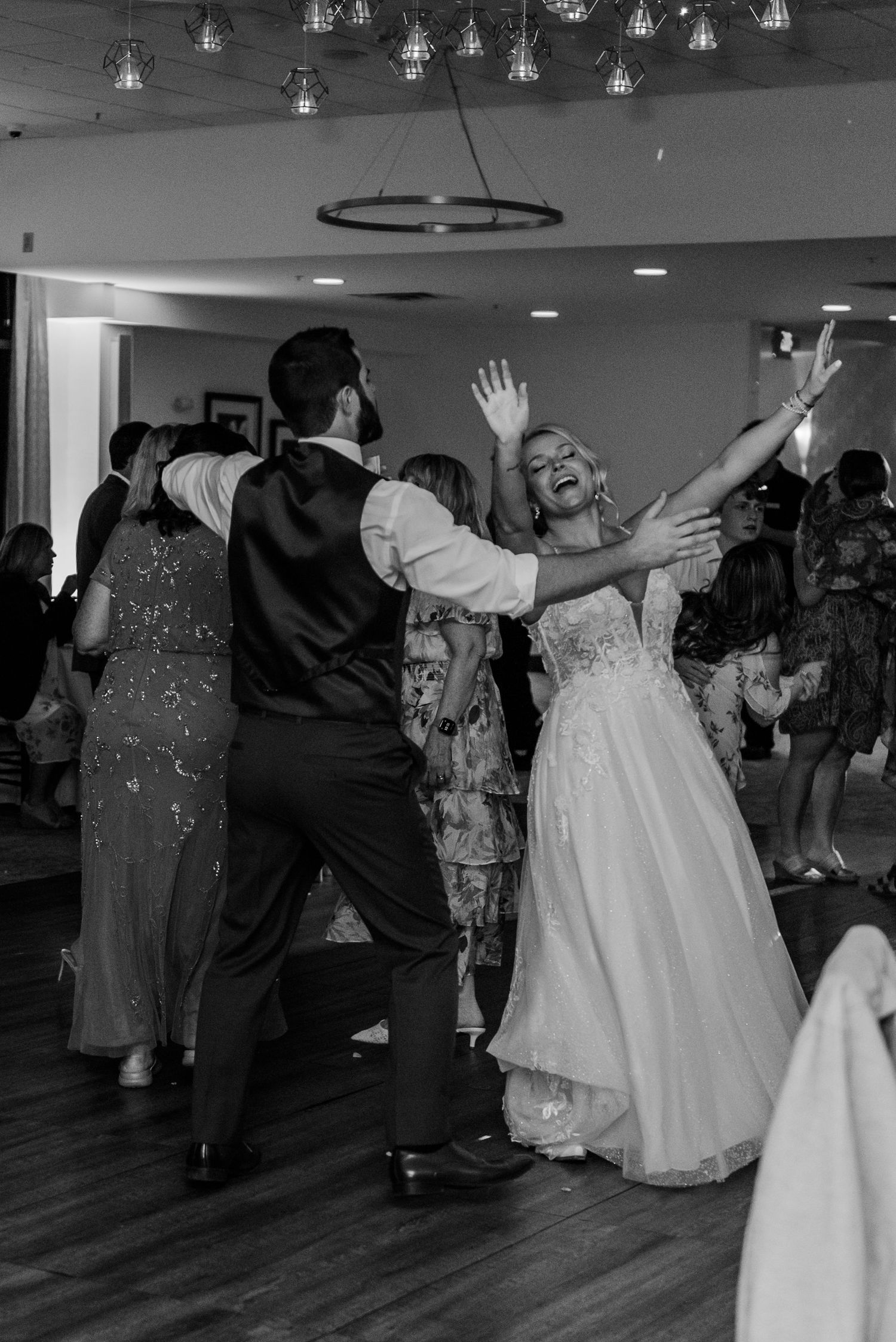Wedding guests dance together in a sequence of black and white photos on a reception dance floor under hanging lights.