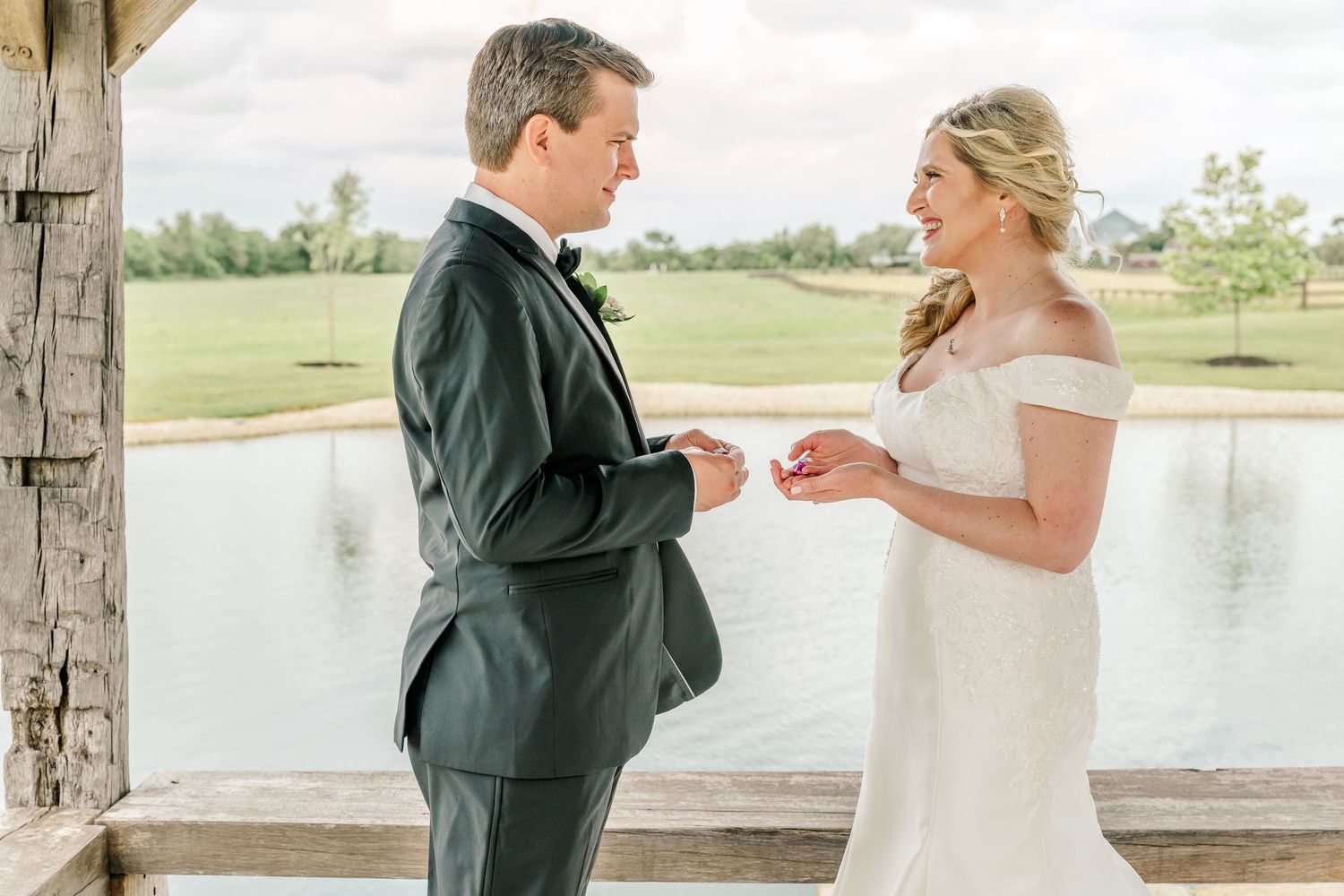 A couple exchanging rings during their wedding ceremony by a lake. The Old Barns at Dry Run Farms in Williamsport, OH.