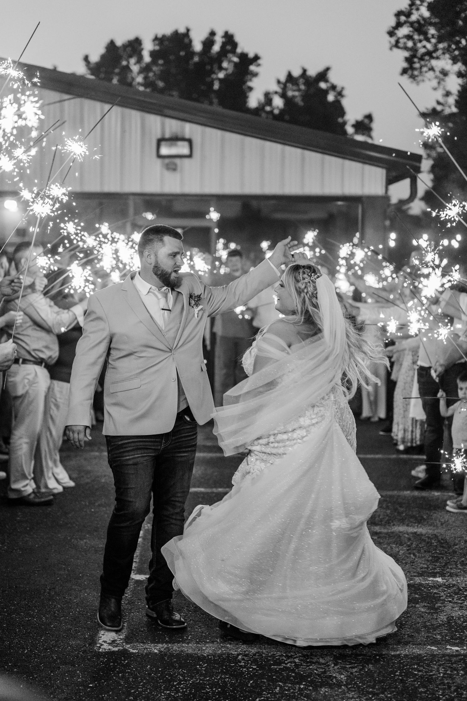 A couple dances and twirls with sparklers at their outdoor wedding reception as the bride's white dress flows elegantly.