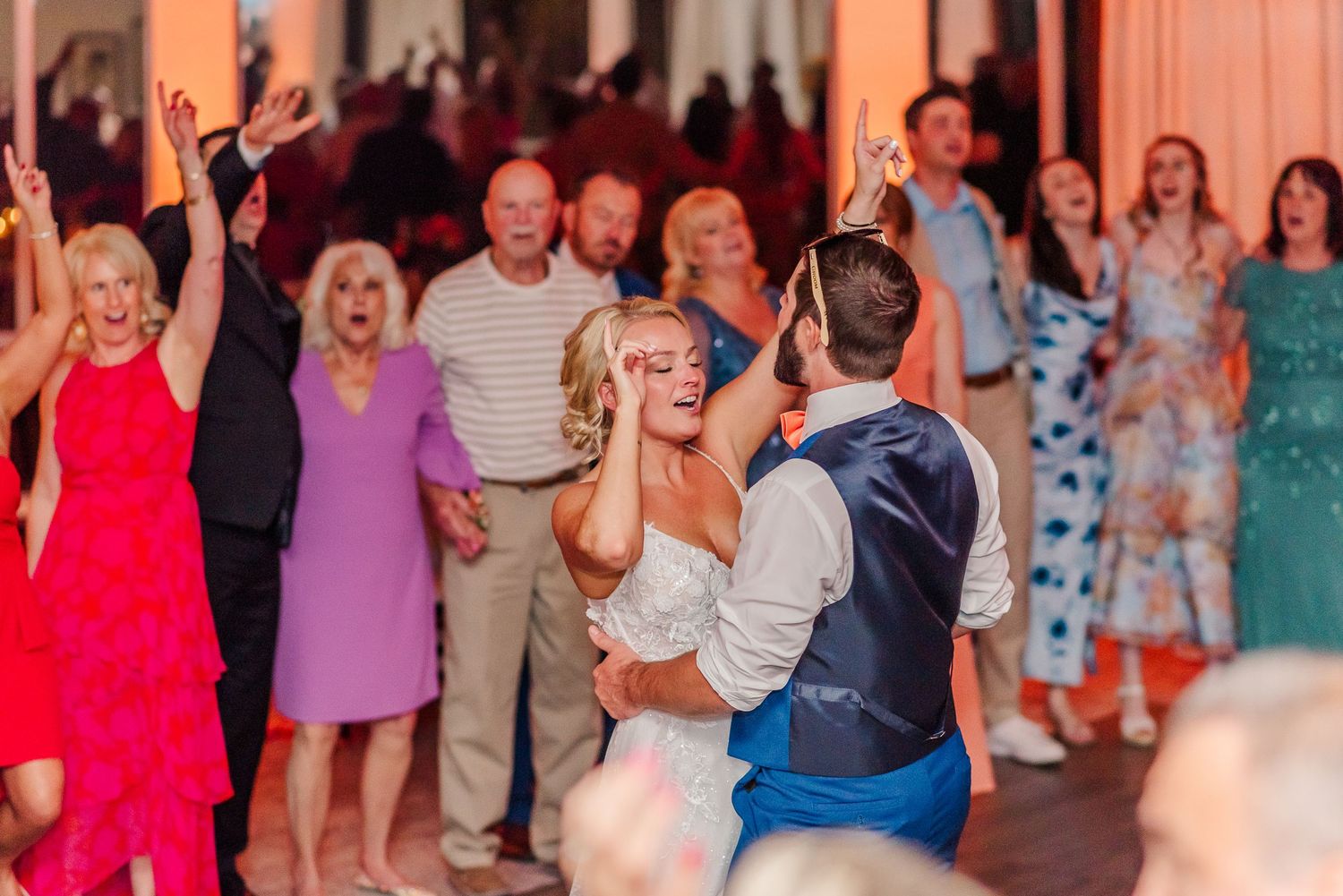 Guests celebrate and dance during a lively wedding reception with warm lighting and festive atmosphere.
