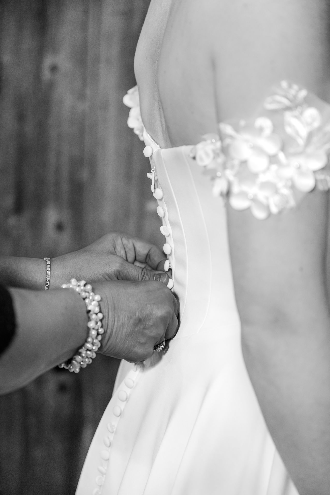 Black and white photo of hands buttoning the back of a bridal gown, with pearl bracelet detail. The Old Barns at Dry Run Farms in Ohio.