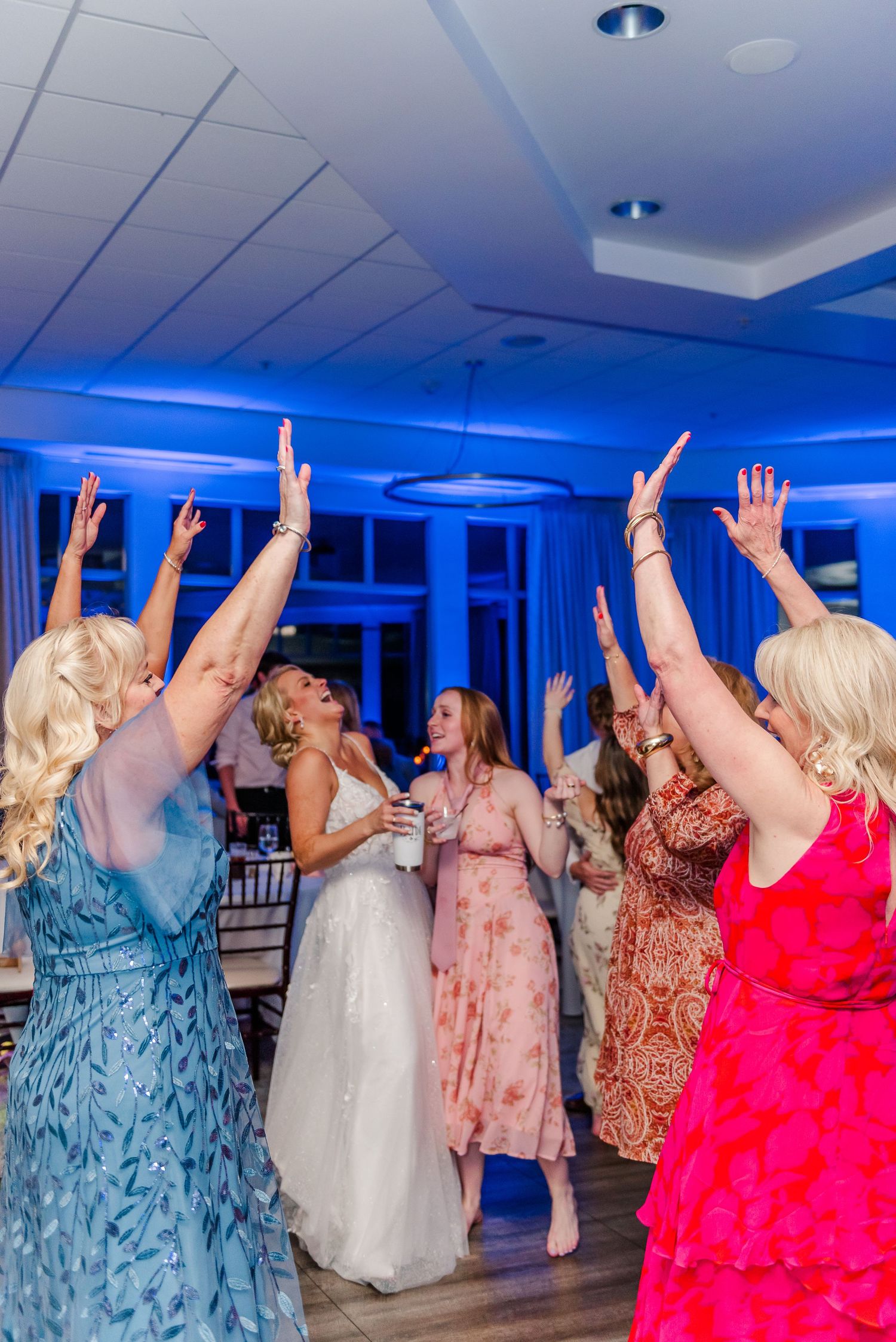 Wedding guests dancing with raised arms under blue lighting on a dance floor.