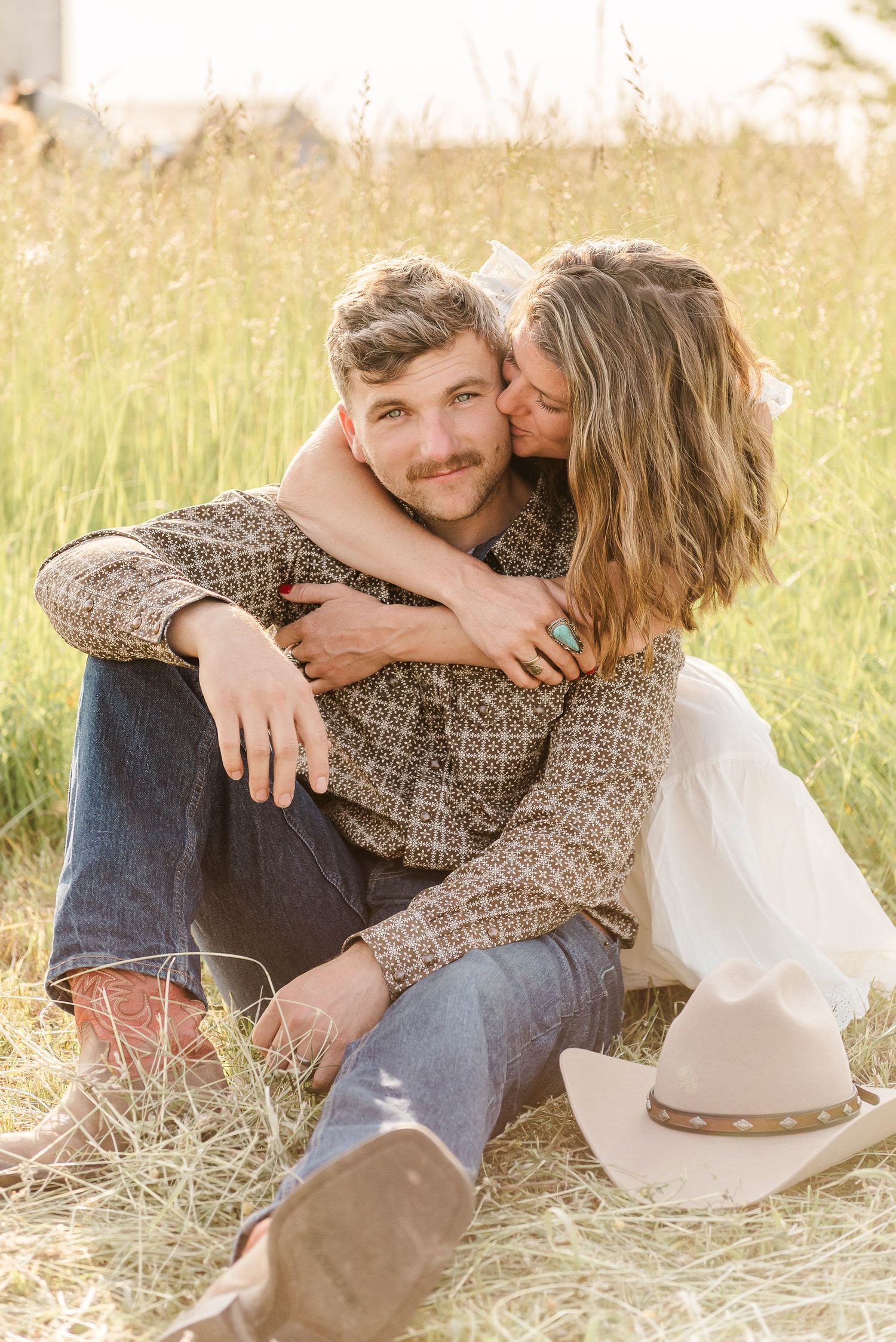 Romantic couple cuddling in a sun-lit meadow with tall grass during a golden hour photoshoot.