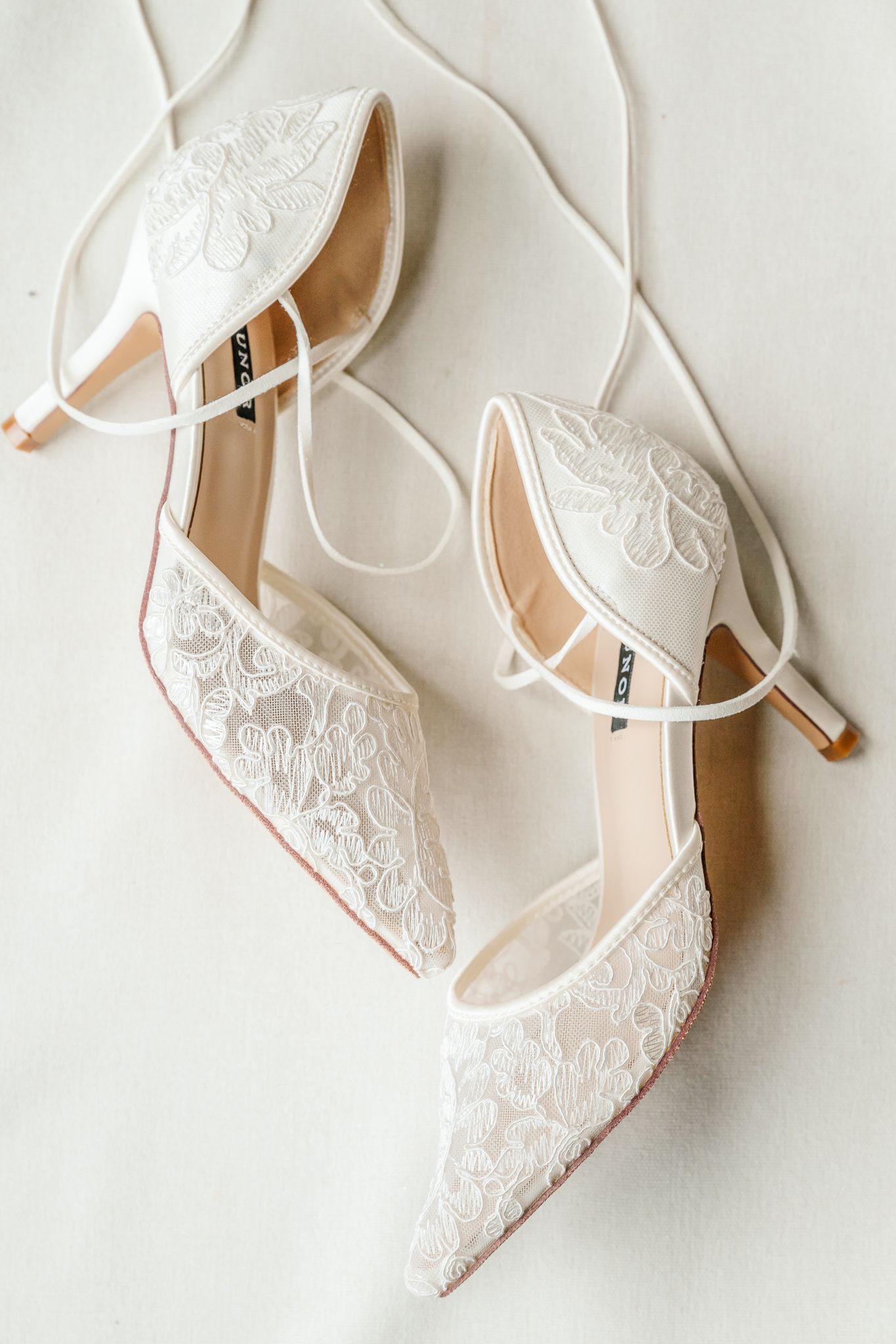 White lace bridal heels with ankle straps and pointed toes displayed on a soft white surface.The Old Barns at Dry Run Farms in Williamsport