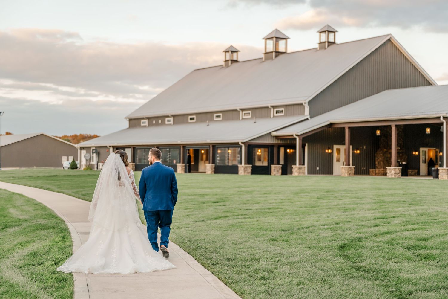 A wedding venue shot showing a rustic barn and green lawn with guests walking outdoors. Four Seasons Barn Wedding & Event Venue