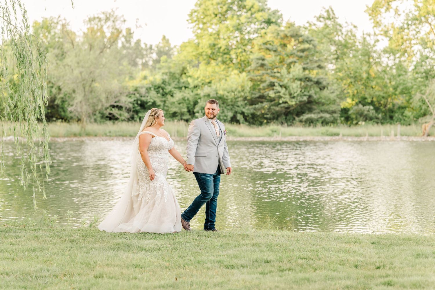 Couple poses together in romantic outdoor photo session near a serene lake with lush greenery in the background.