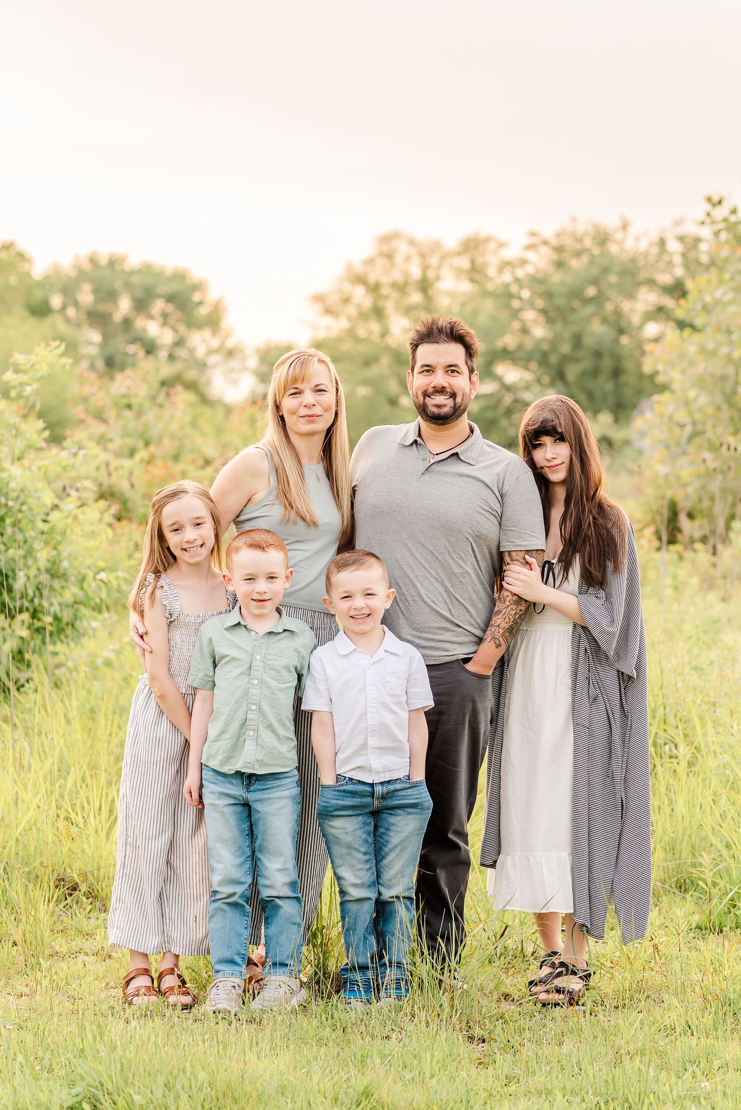 A family stands together in a scenic meadow during a warm summer evening.