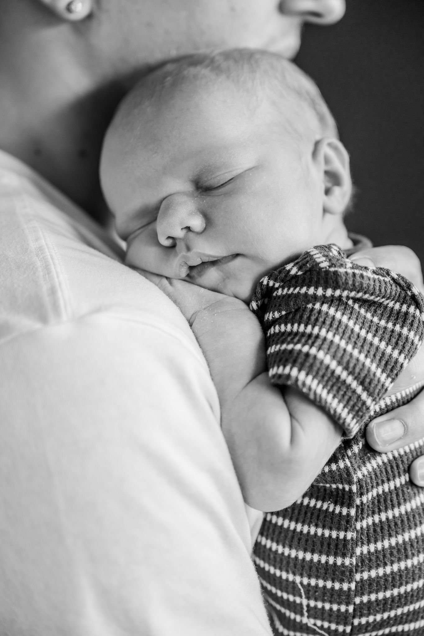 Black and white photo of a sleeping newborn baby cradled in a parent's arms, wearing a striped outfit.