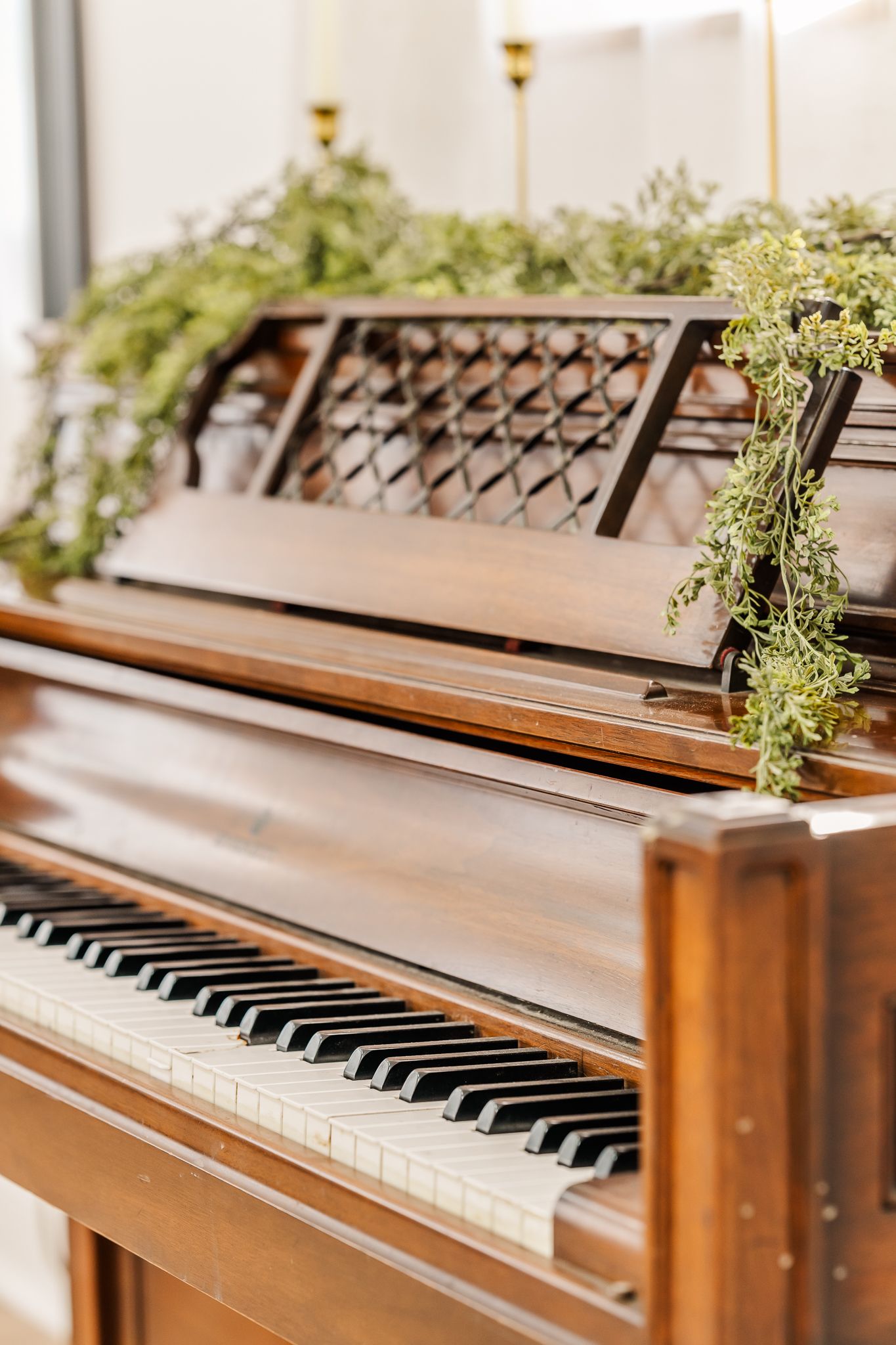 Vintage wooden piano with decorative greenery on top showcasing black and white keys in warm natural lighting.