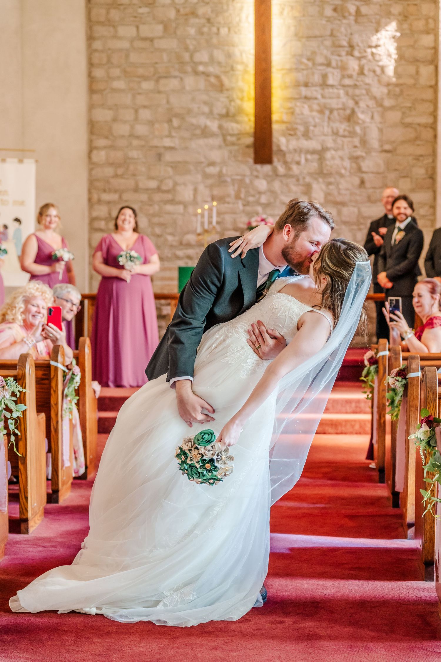 Dramatic dip pose during first dance in stone-walled church with red carpet and pews.