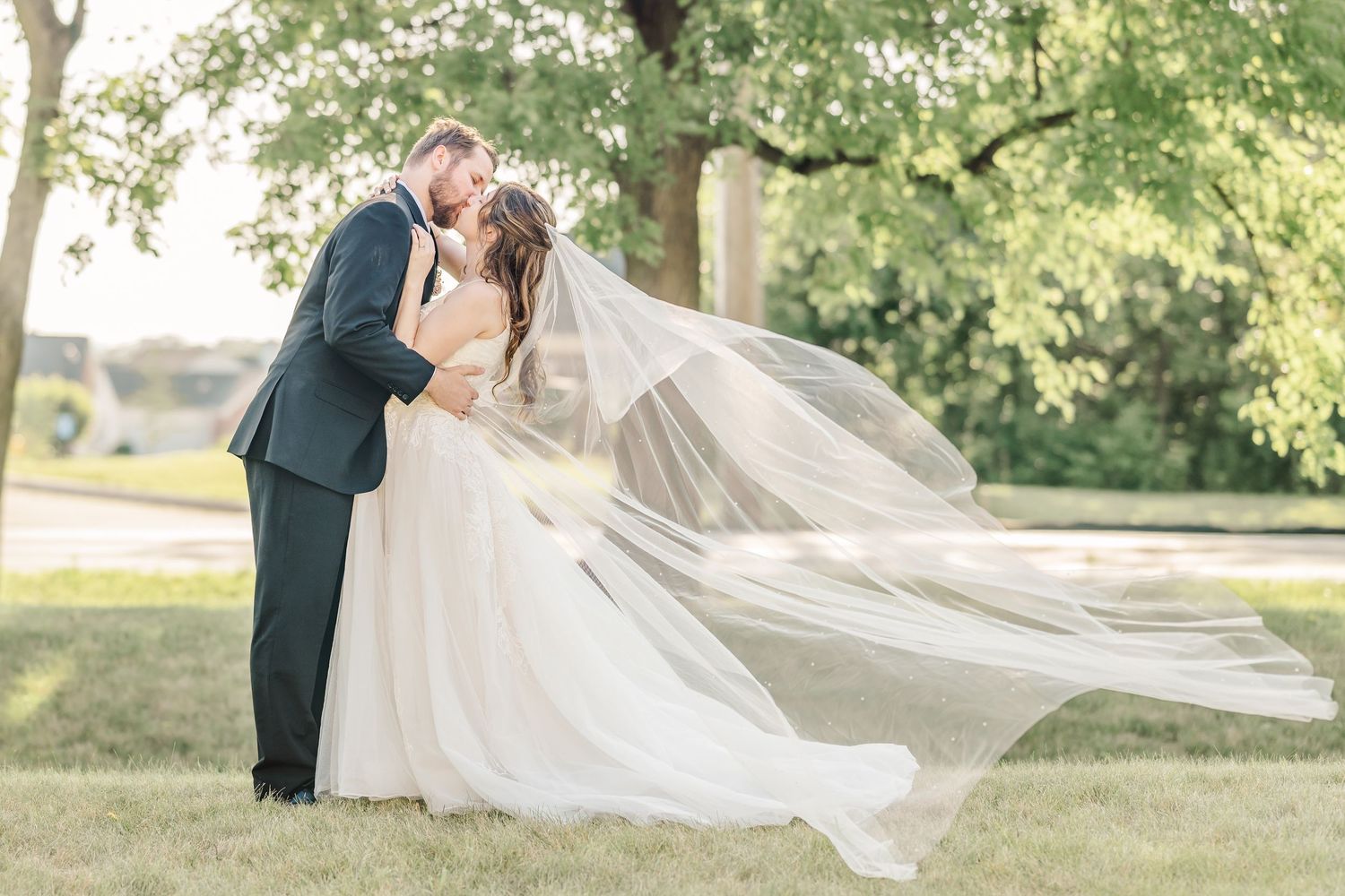 A flowing white wedding veil catches the breeze in a sunlit garden setting during a romantic outdoor photoshoot.