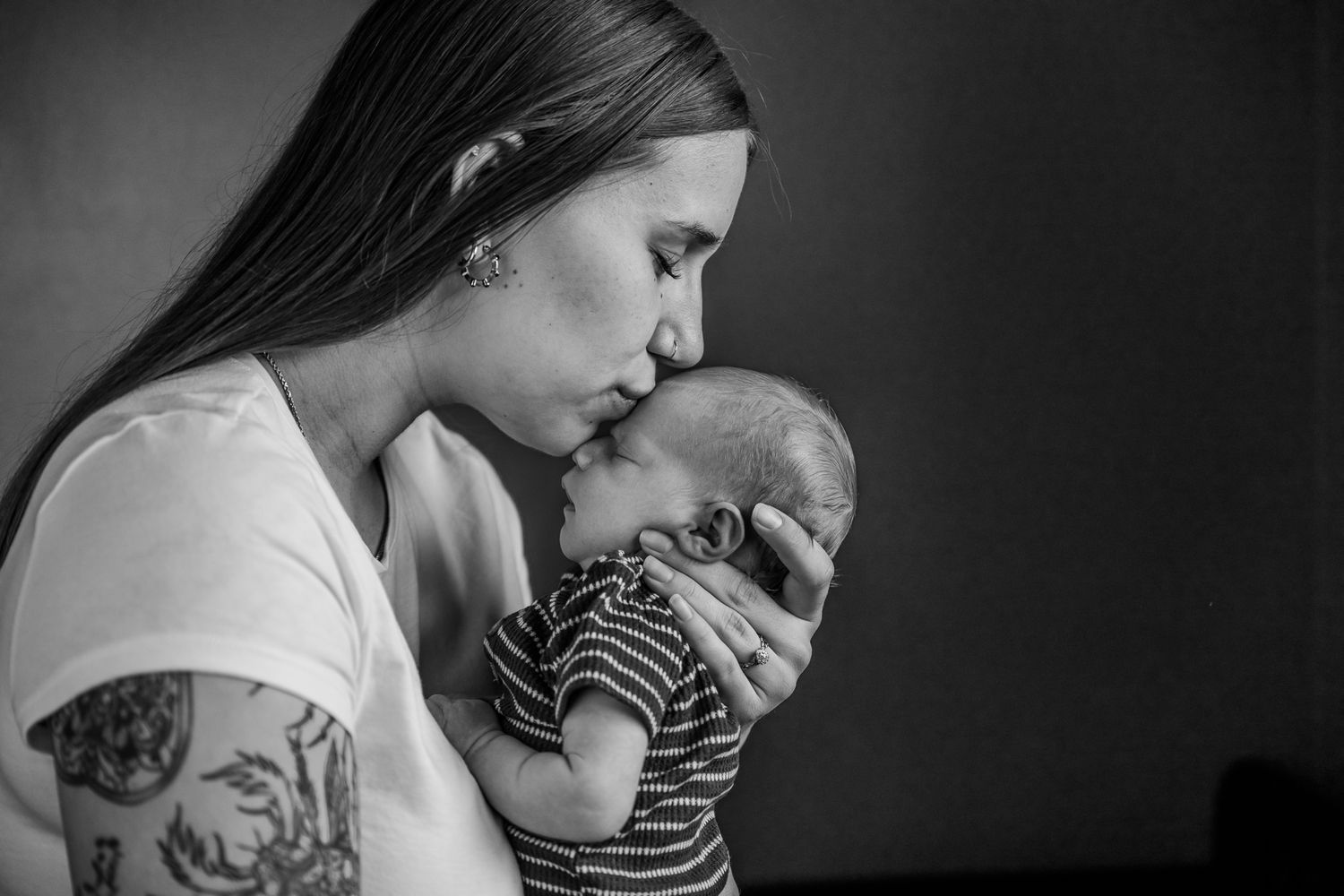 Black and white photo of a tattooed mother gently kissing her newborn baby.