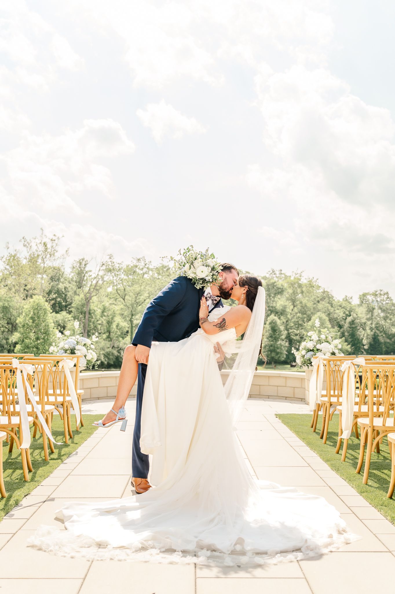 Groom dips bride for a kiss at outdoor wedding ceremony aisle flanked by wooden chairs and lush greenery Canopy Creek Farm wedding venue