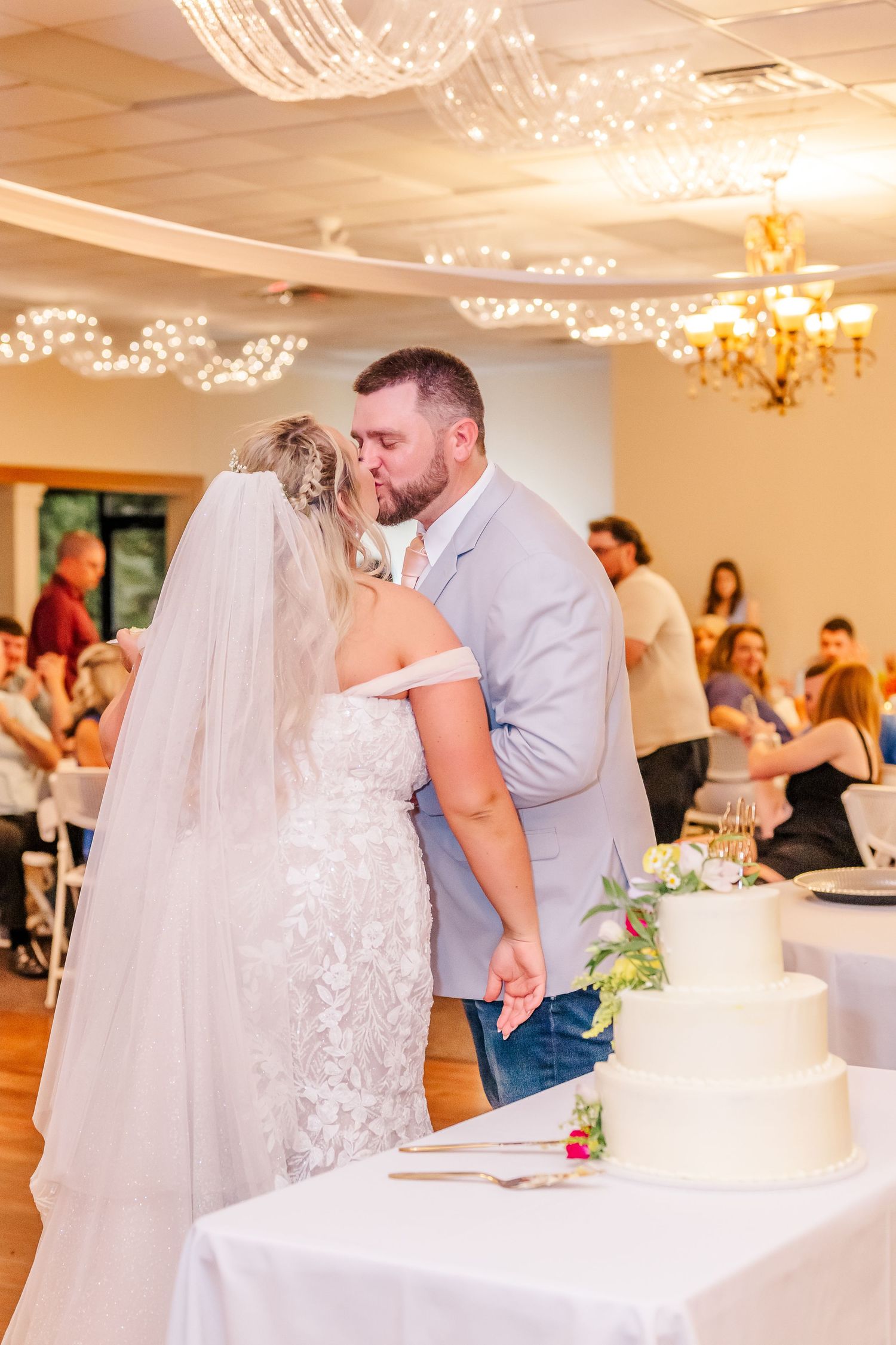A romantic wedding reception scene with string lights and chandeliers illuminating couples dancing on the dance floor.