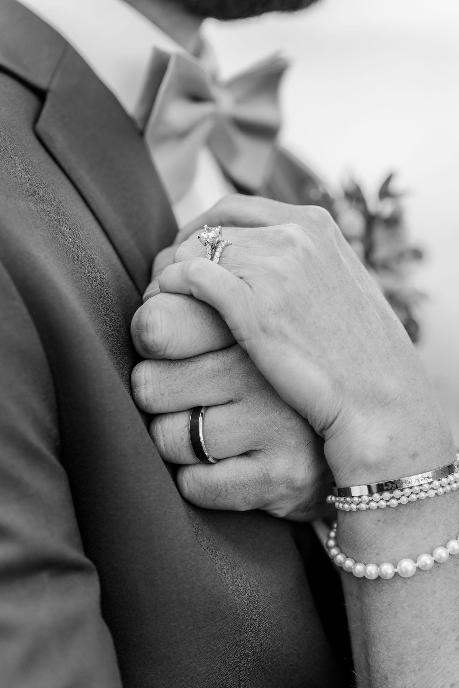 Black and white close-up photos of clasped hands wearing wedding rings and pearl bracelets showing tender moments.