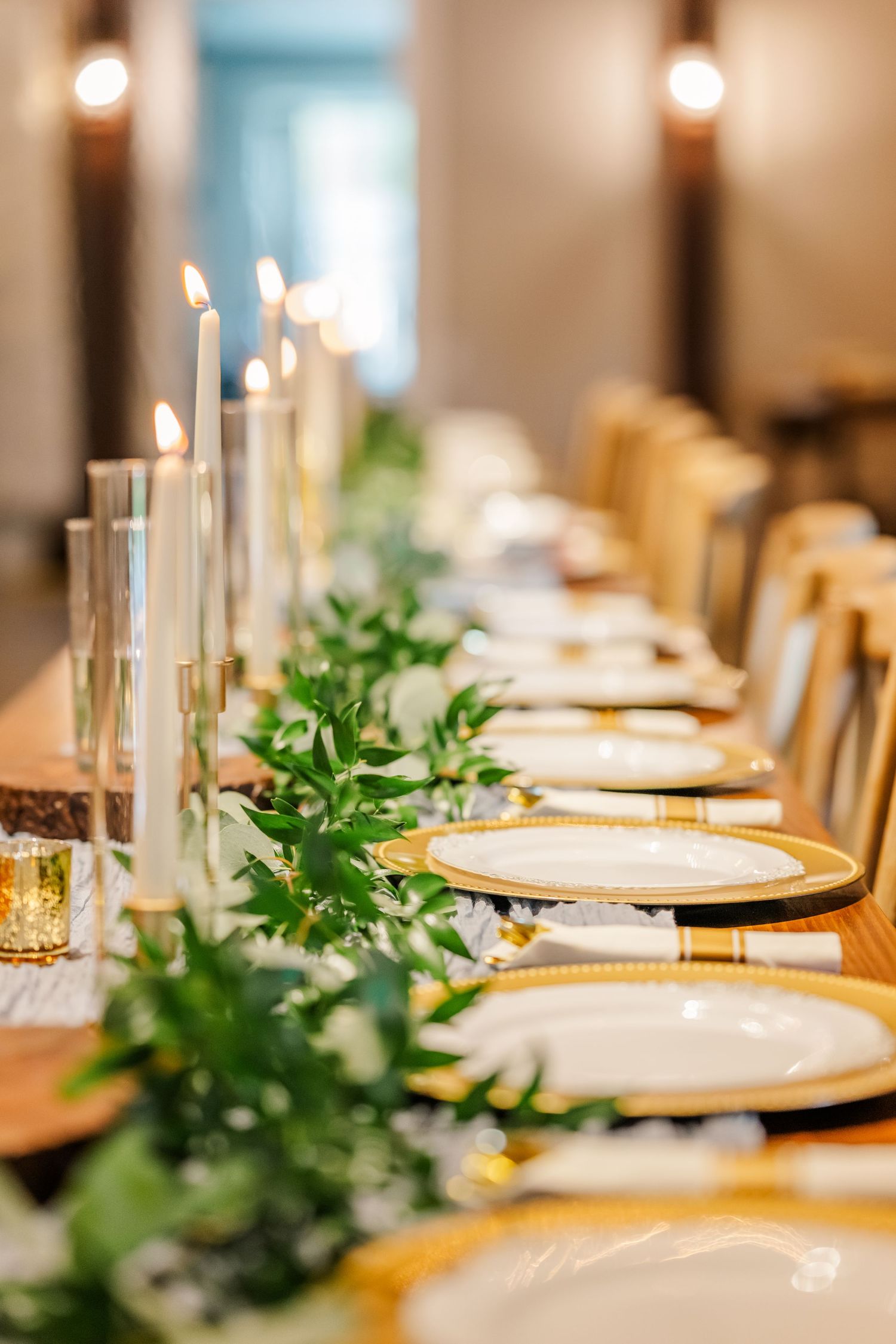 Elegant table setting with white plates, taper candles, and fresh greenery garland for a formal dining event.Four Seasons Barn Wedding