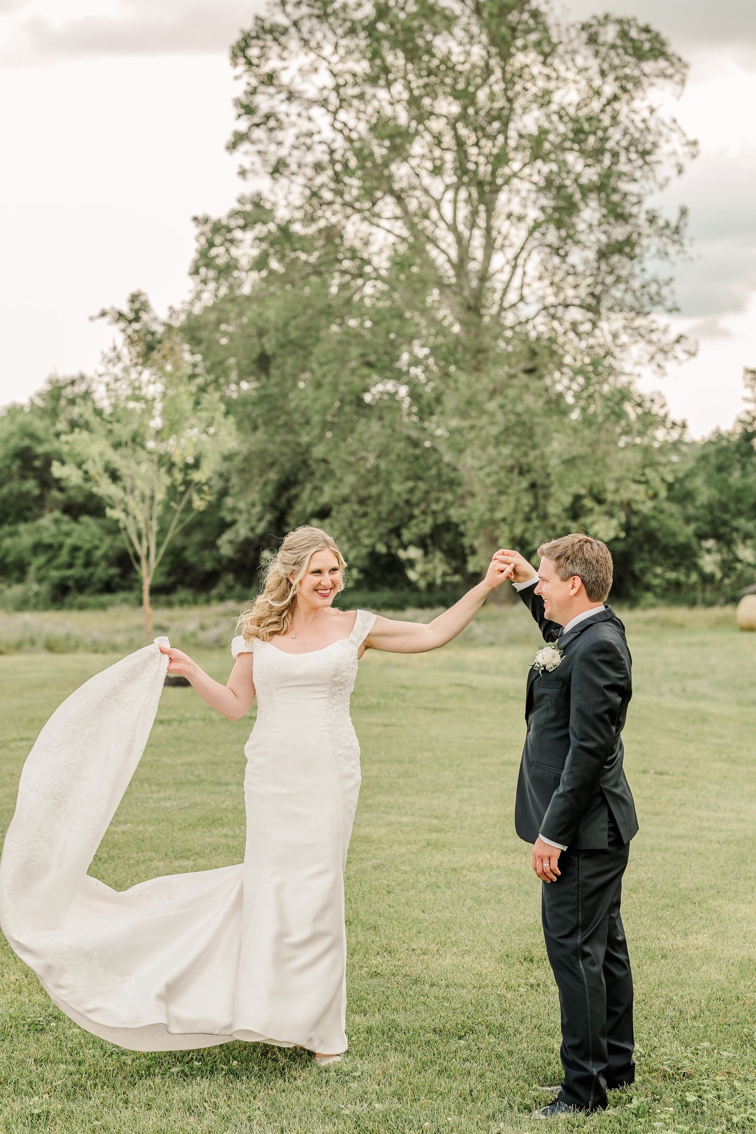 A couple dances in a lush green field as the bride's elegant white dress and veil flow in the breeze.The Old Barns at Dry Run Farms