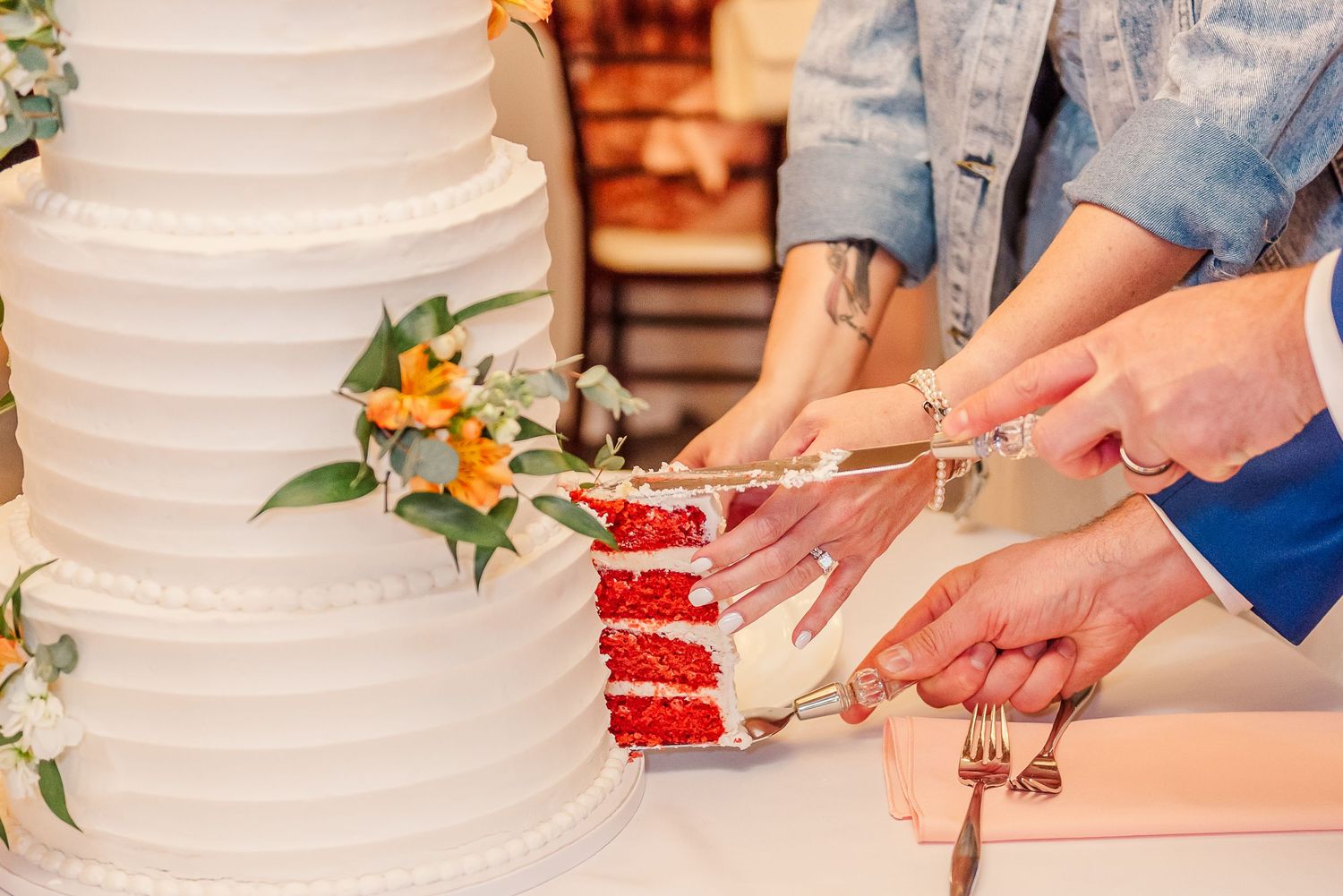 A white wedding cake being cut into slices with a knife showing layers of red velvet cake inside.