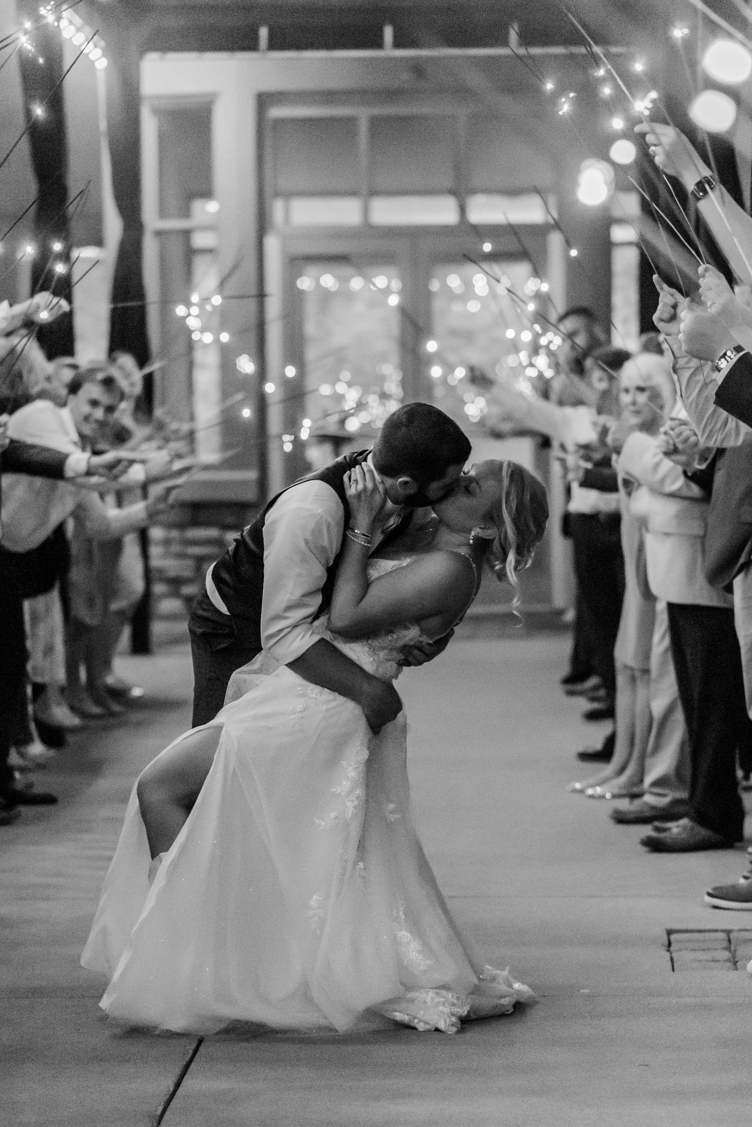 A romantic sparkler exit with a couple sharing a kiss while guests line the walkway with lit sparklers.