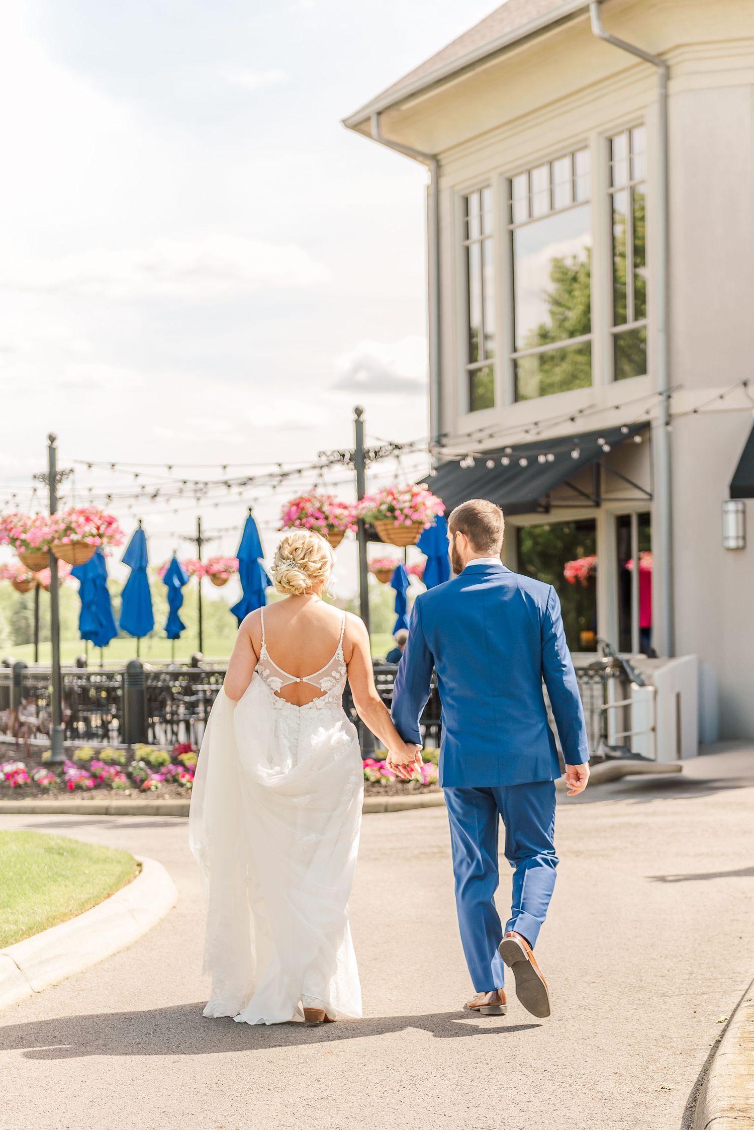 A couple walks together on a sunny day at an outdoor venue decorated with string lights and blue banners.