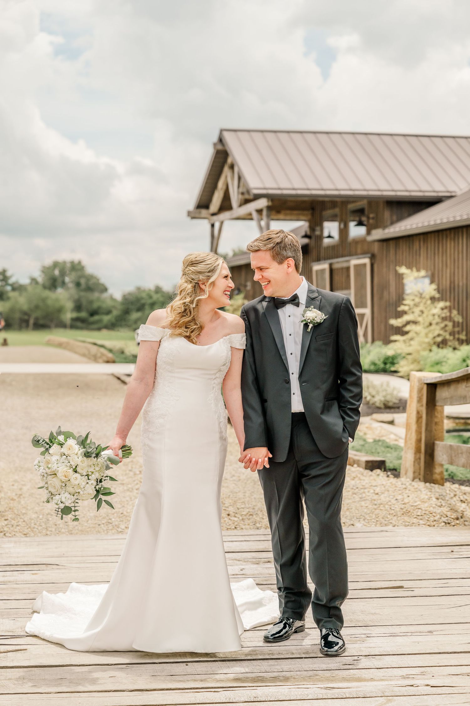 Wedding couple shares intimate moment on rustic wooden deck with barn buildings in background.