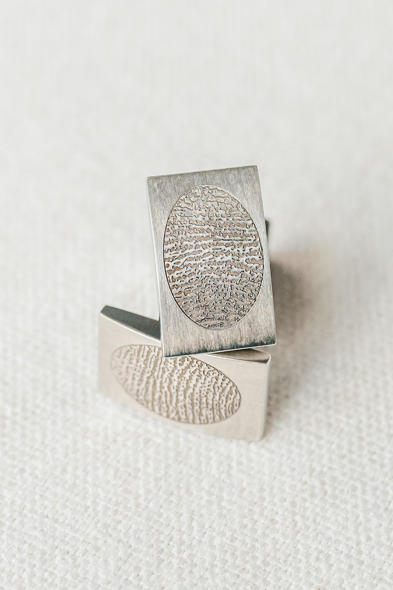 Silver fingerprint jewelry stamp showing detailed ridge patterns on a textured white background.