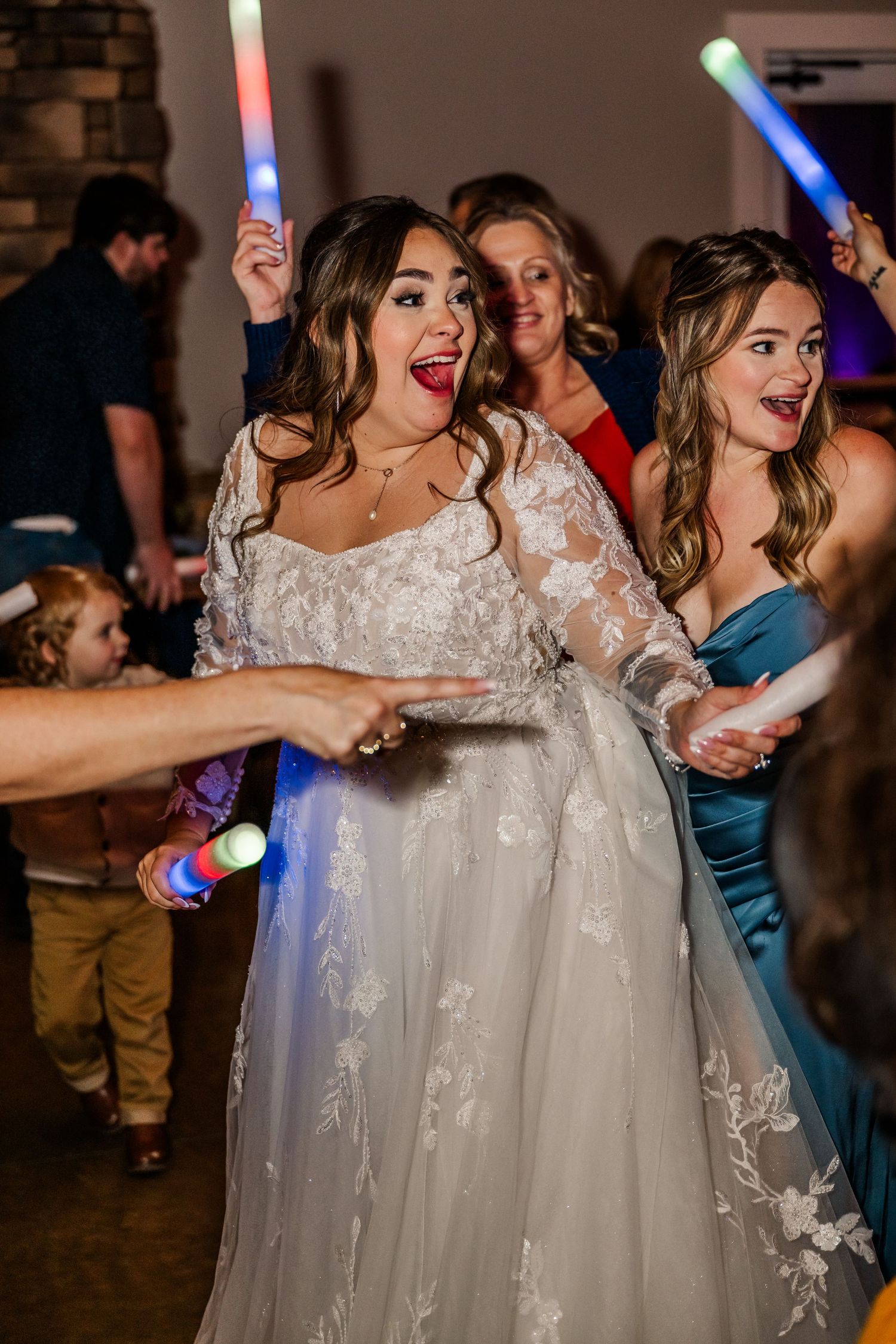 Wedding guests dance together on the dance floor during a reception celebration with colorful lighting.Four Seasons Barn Wedding