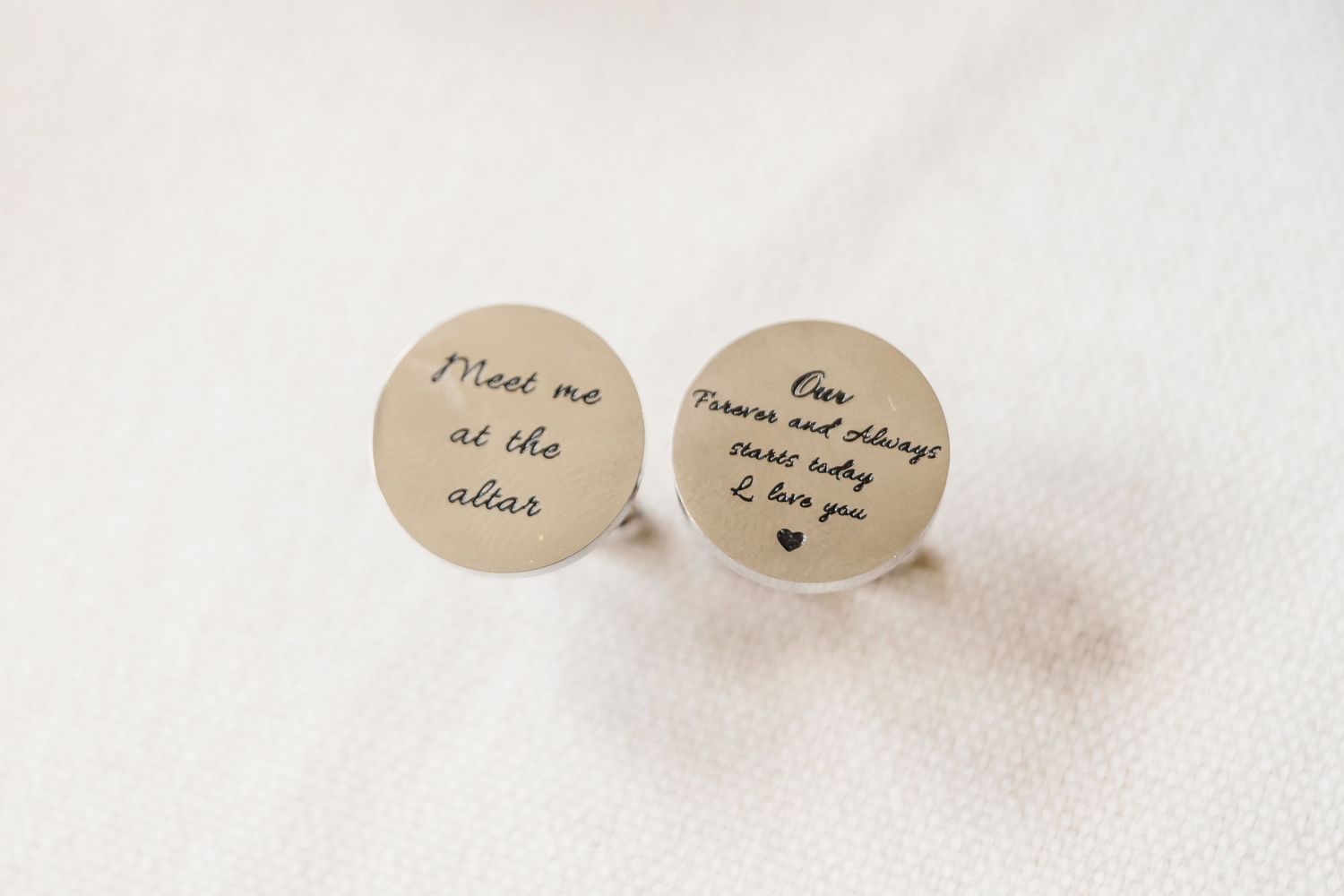 Small silver stud earrings with engraved text and heart designs on a white background.