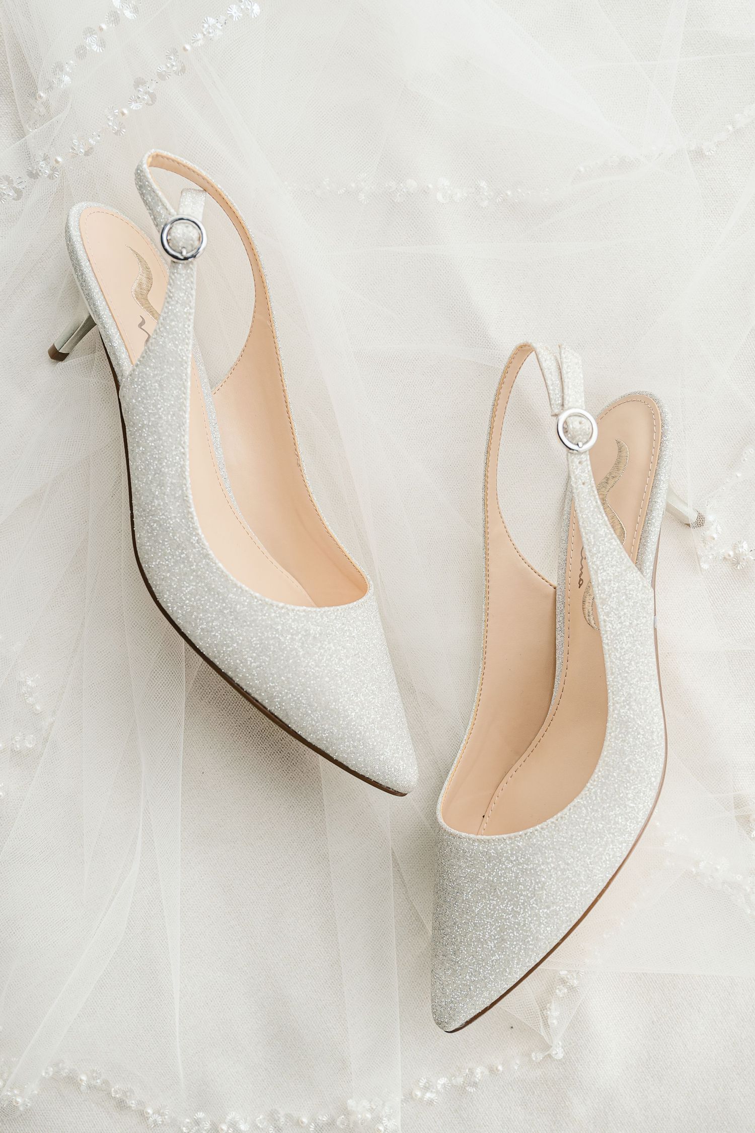 Elegant white glitter slingback kitten heels with pointed toes and delicate buckle details on a light background.