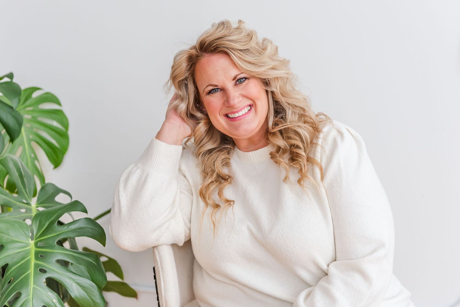 Portrait session in white studio setting with bright natural lighting and monstera plant decor.