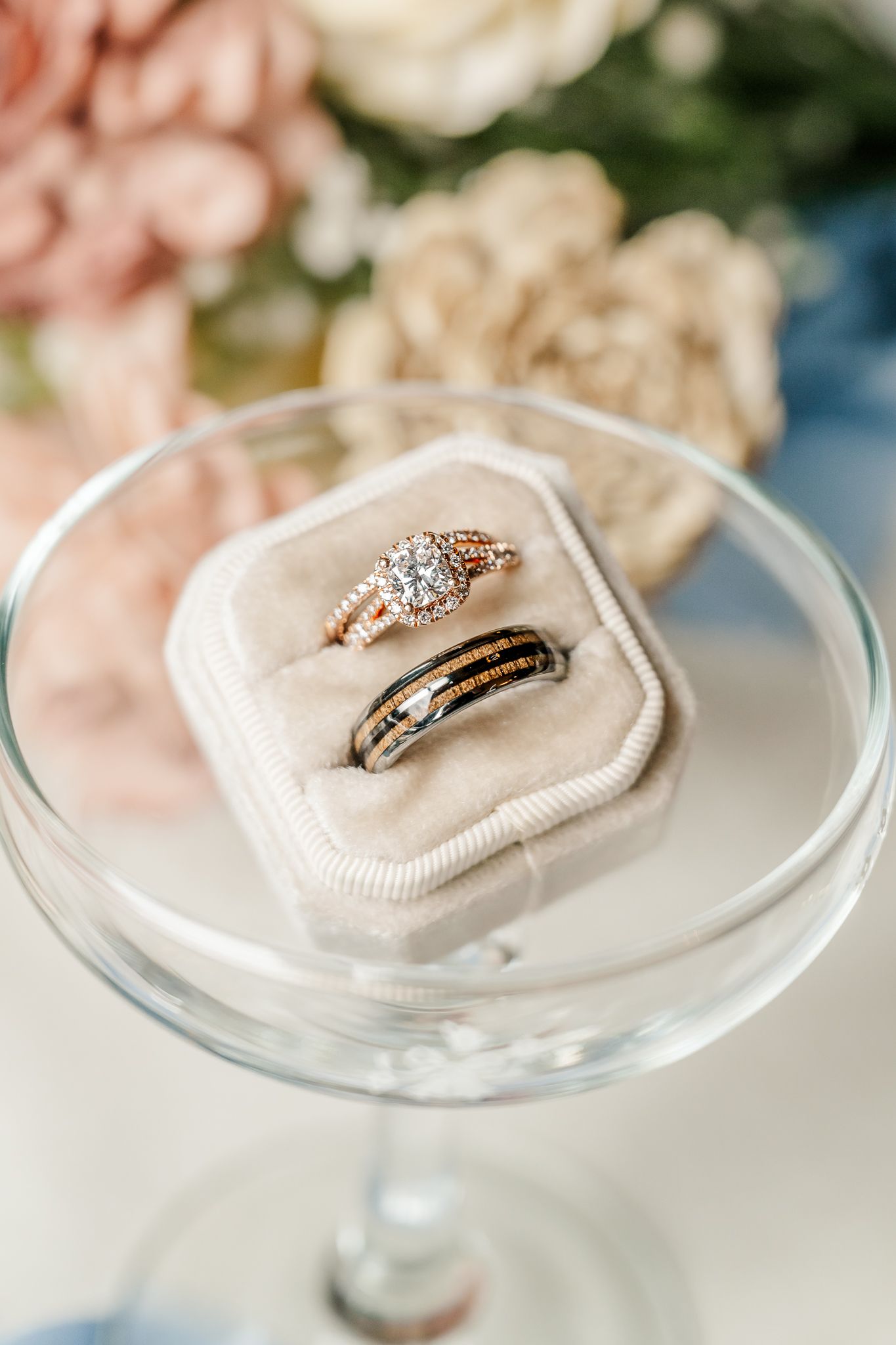 Two wedding rings in a velvet box on a glass stand, with a diamond engagement ring and a dark wood band. The Old Barns at Dry Run Farms