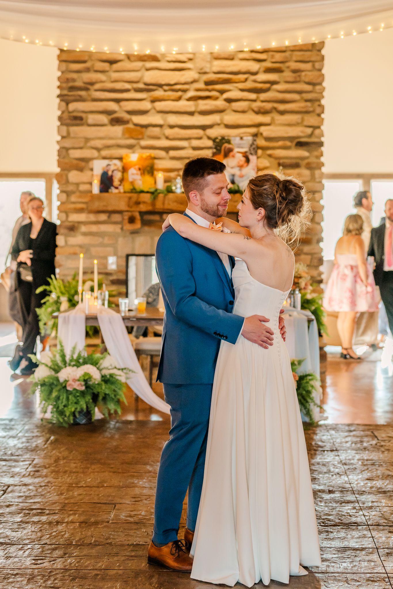 Bride and groom share their first dance in a rustic stone venue decorated with fairy lights and floral arrangements.