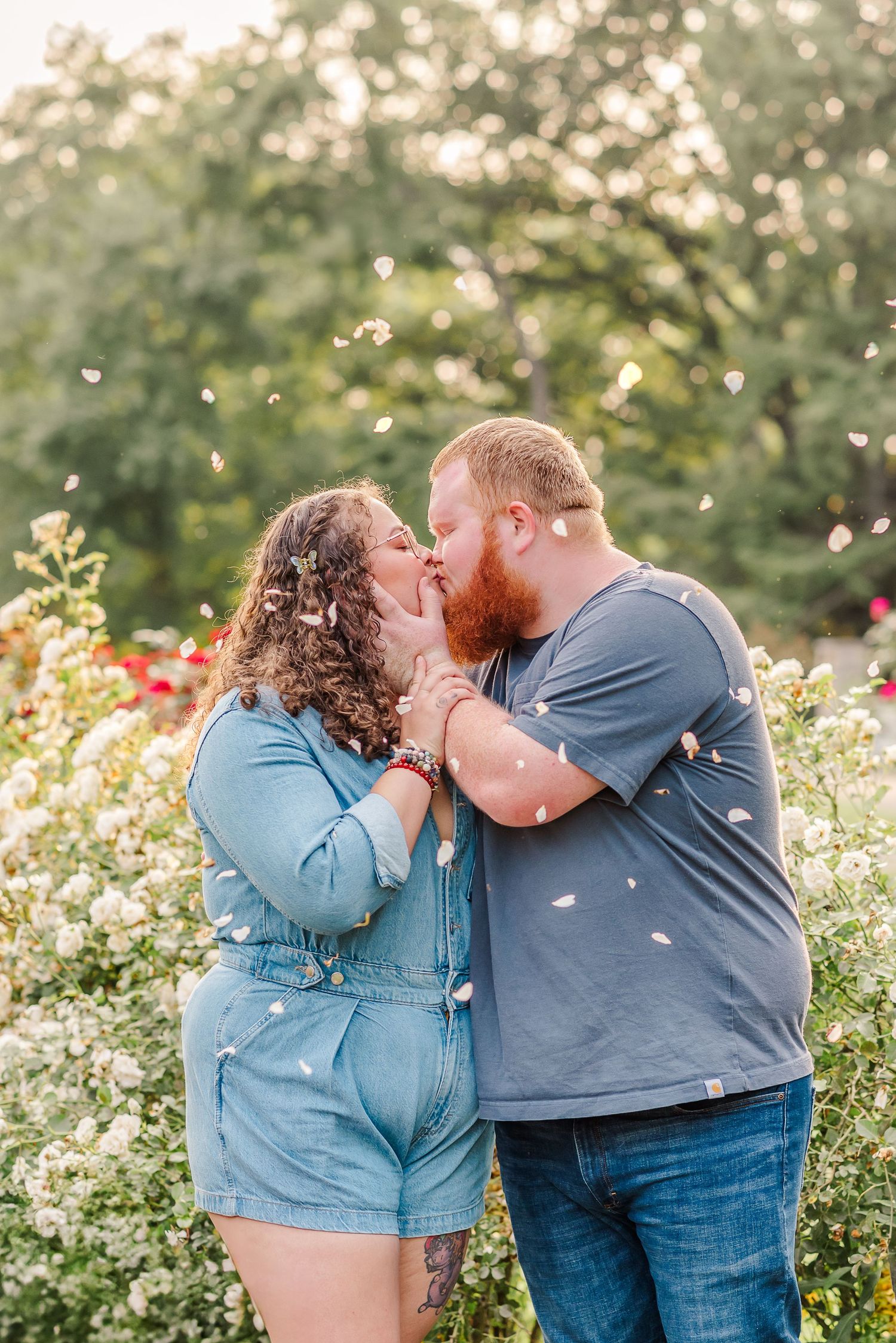 Couple sharing romantic moment amid blooming flower garden with petals falling.