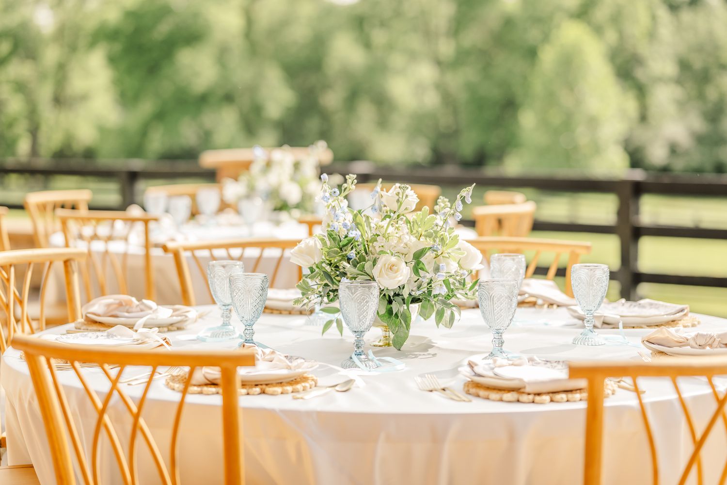 Elegant outdoor wedding reception table with white linens, gold chairs, floral centerpiece, and blue glassware. Canopy Creek Wedding Venue