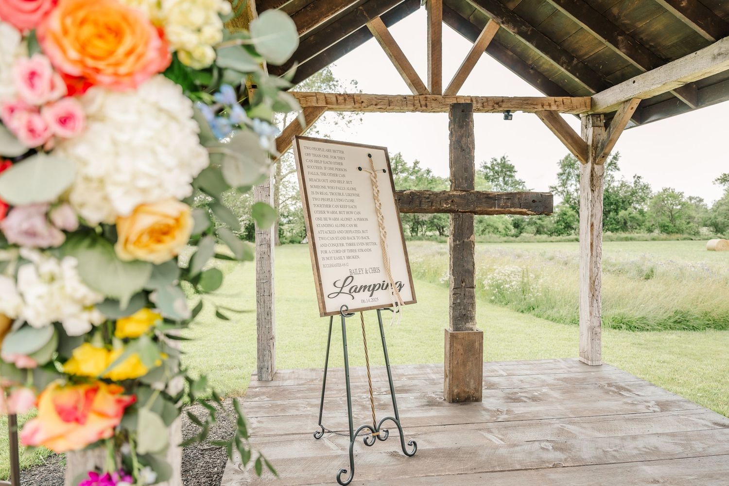 Rustic wooden pavilion decorated with colorful floral arrangements and wedding signage at The Old Barns at Dry Run Farms in Williamsport