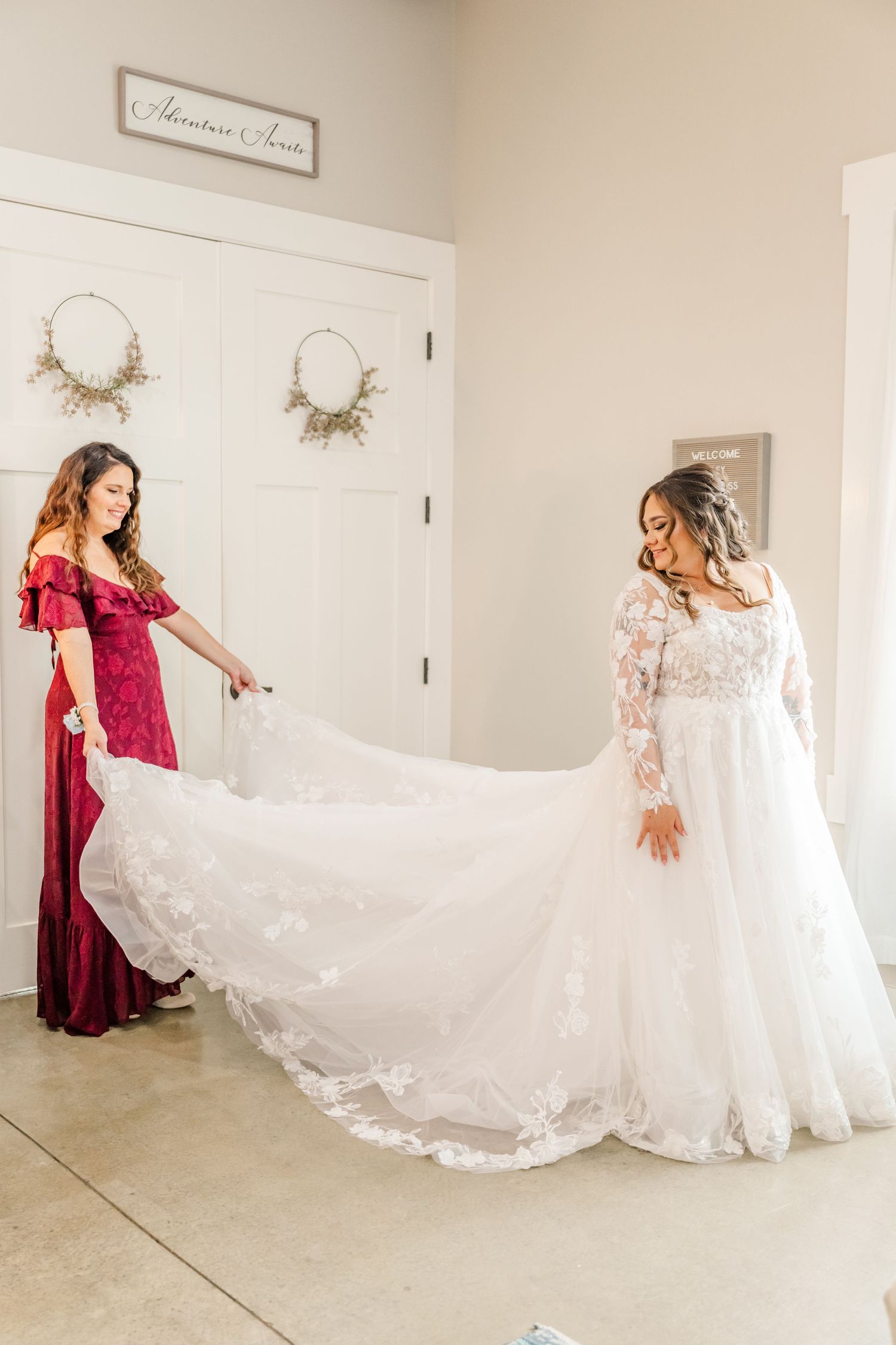 A wedding dress with long lace sleeves & flowing train being displayed in a bridal preparation room.Four Seasons Barn Wedding & Event Venue