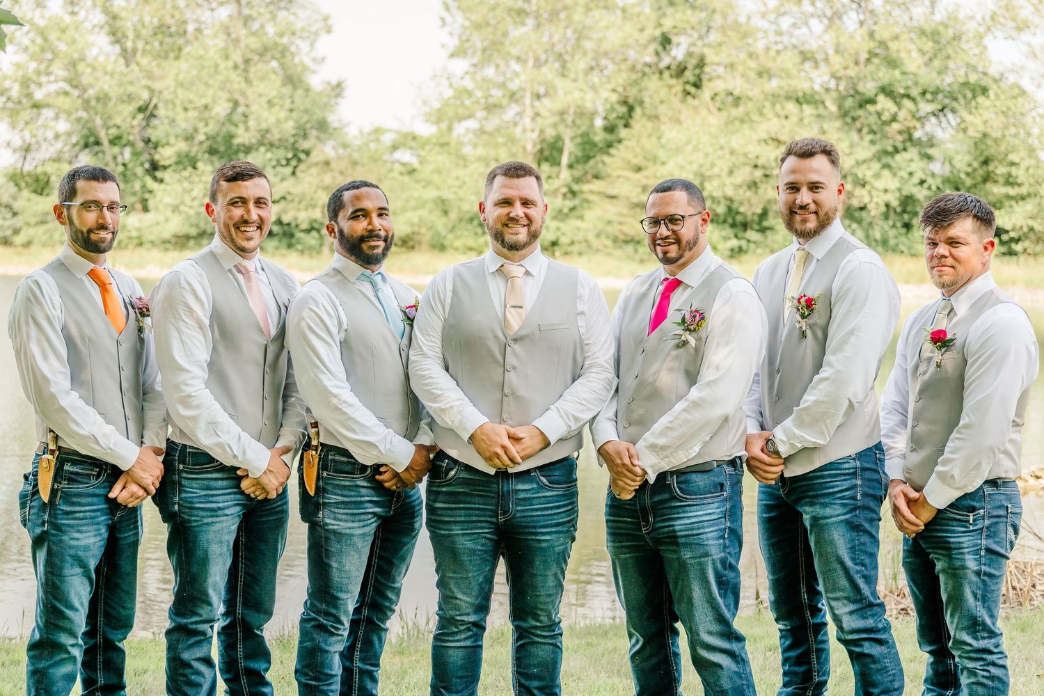 Groomsmen in matching emerald green pants and light gray dress shirts pose together outdoors in a garden setting.